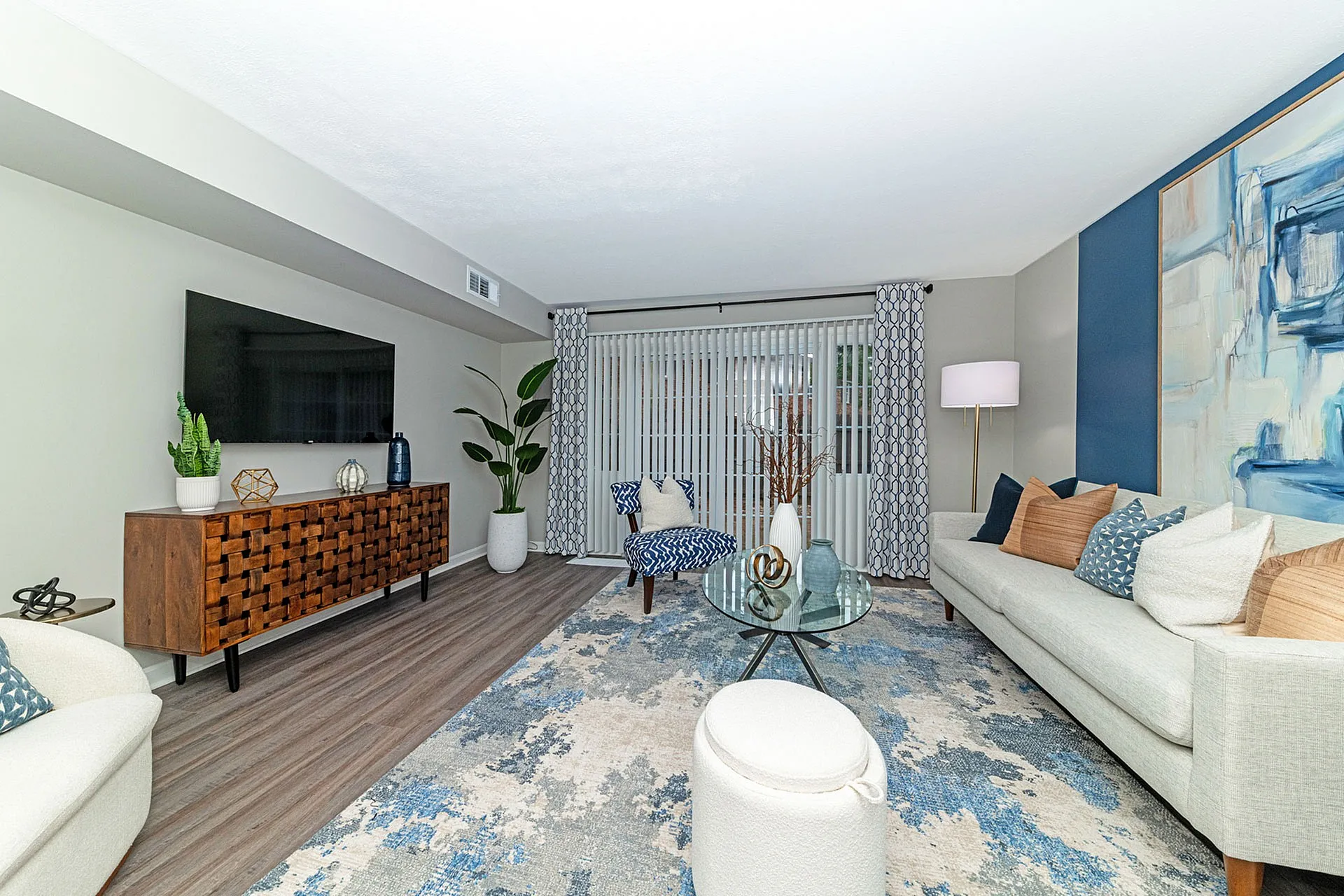 Elegant modern living room with stylish decor, featuring a plush ivory sofa, vibrant artwork, and a chic wooden console. Inviting natural light through large patio doors creates a warm, cozy atmosphere.