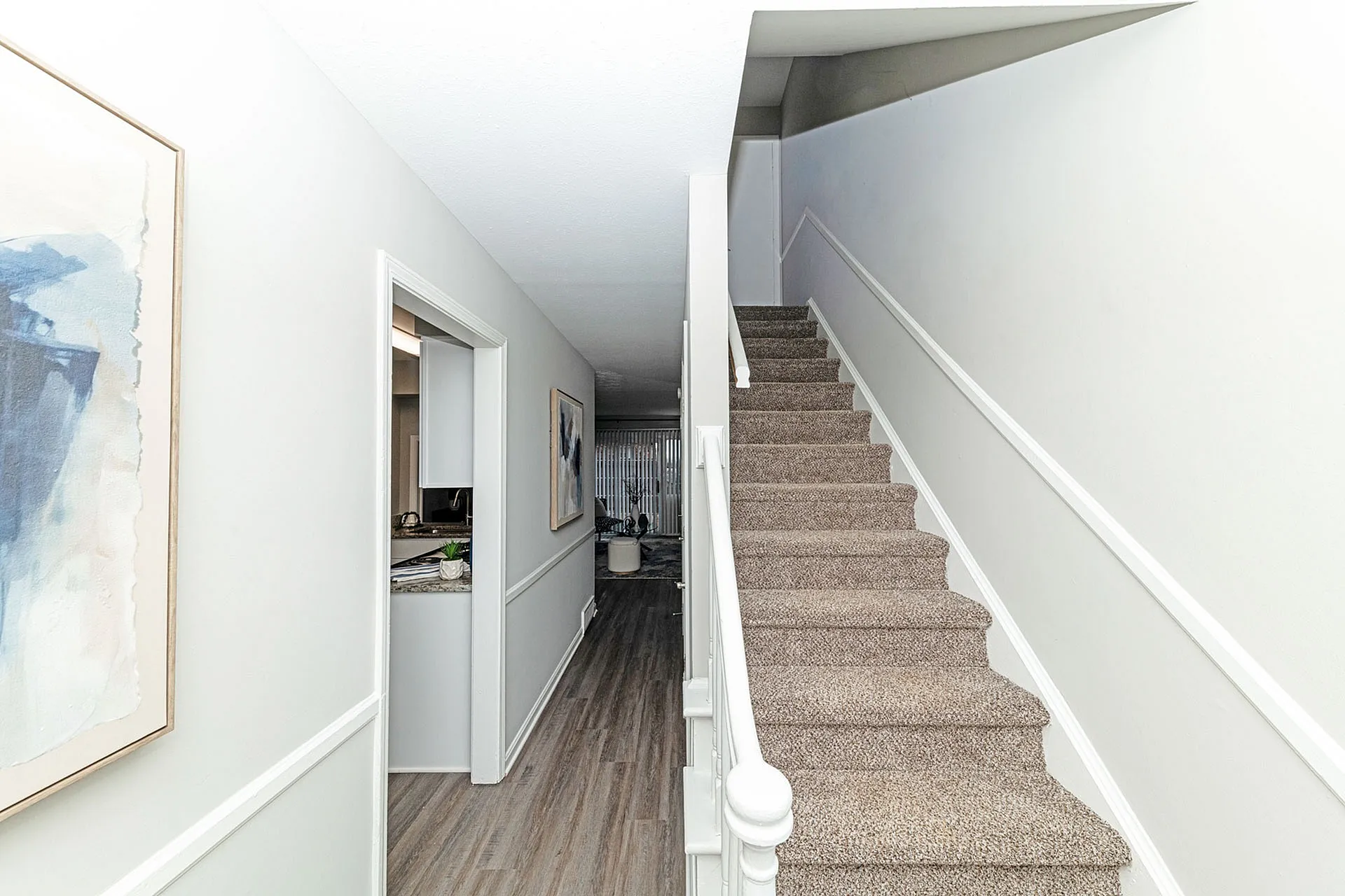 Inviting hallway with elegant staircase and sleek gray laminate flooring, leading to a cozy living area that ensures a warm welcome home.