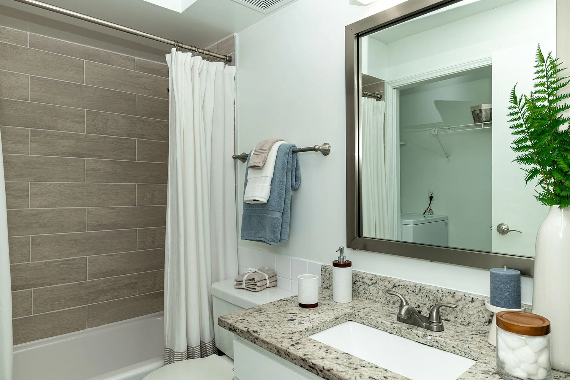 Modern bathroom with sleek granite countertop, stylish mirror, and elegant tile bathtub. Accented with plush towels and vibrant greenery, offering a luxurious and inviting atmosphere.