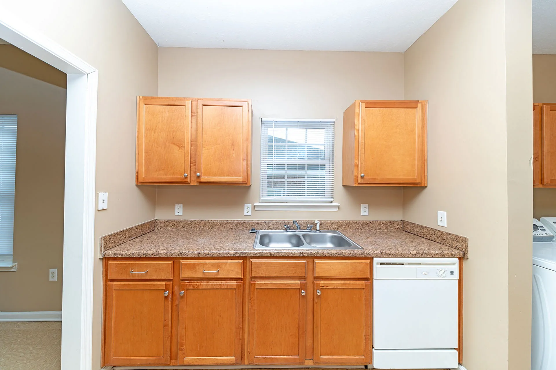 Inviting kitchen space with warm wooden cabinets, elegant granite countertops, double sink, and modern dishwasher, offering functionality and style.