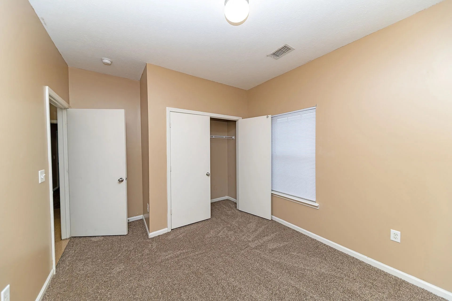 Bright and welcoming room with warm beige walls, cozy carpet, and ample closet space, perfect for a comfortable living area.