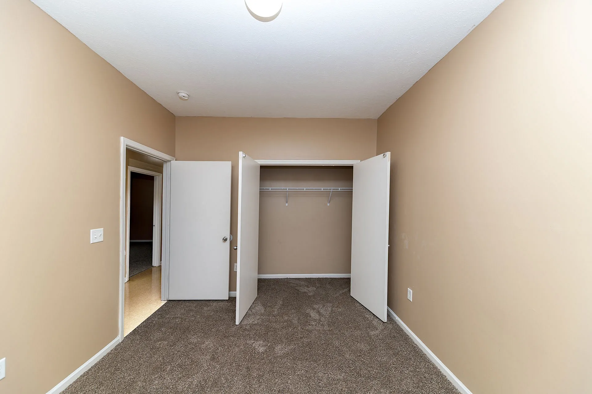 Inviting bedroom featuring a plush carpet, neutral walls, and an ample closet space with open doors.