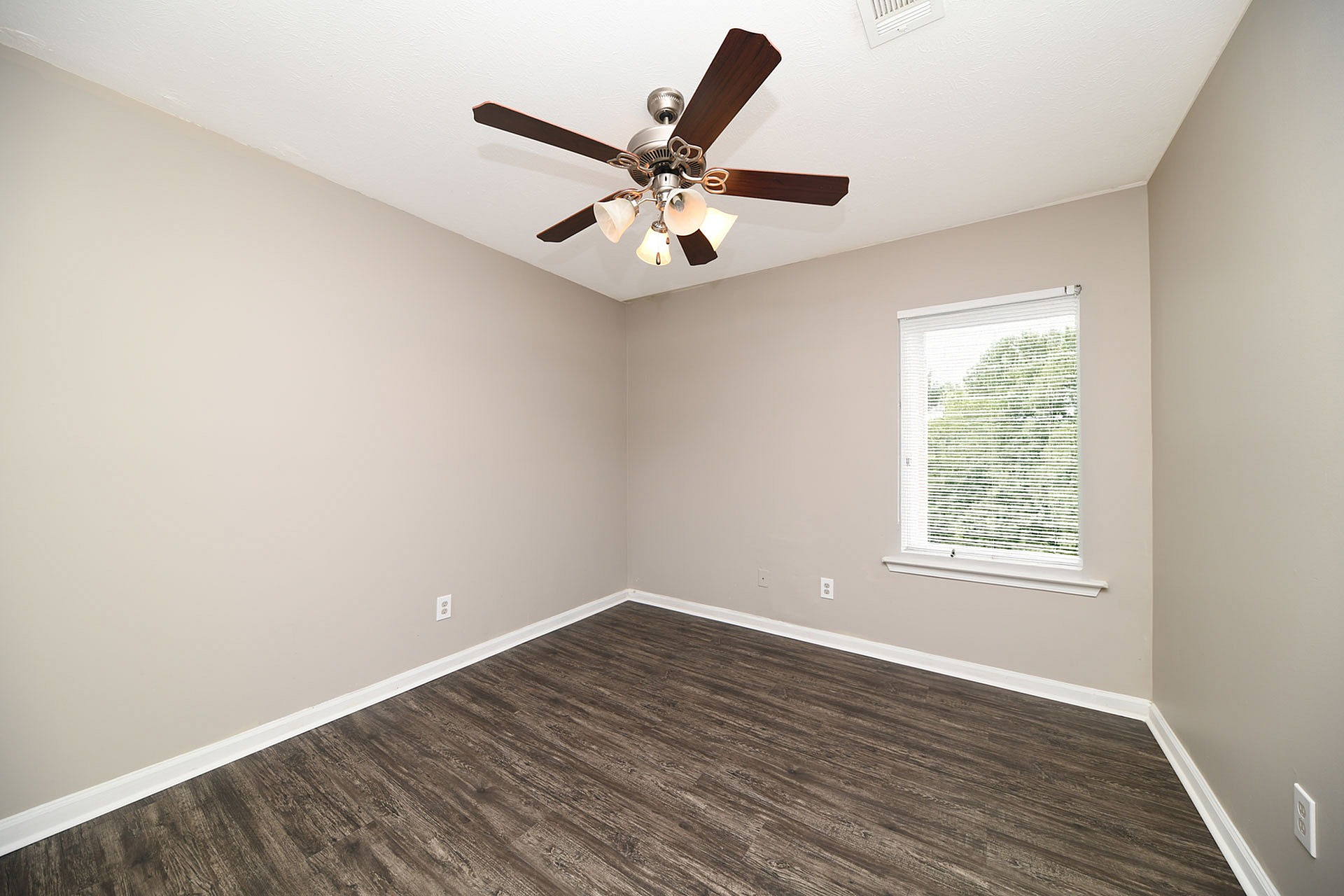 Bright room with elegant dark wood flooring, neutral walls, and a ceiling fan in a peaceful apartment setting.