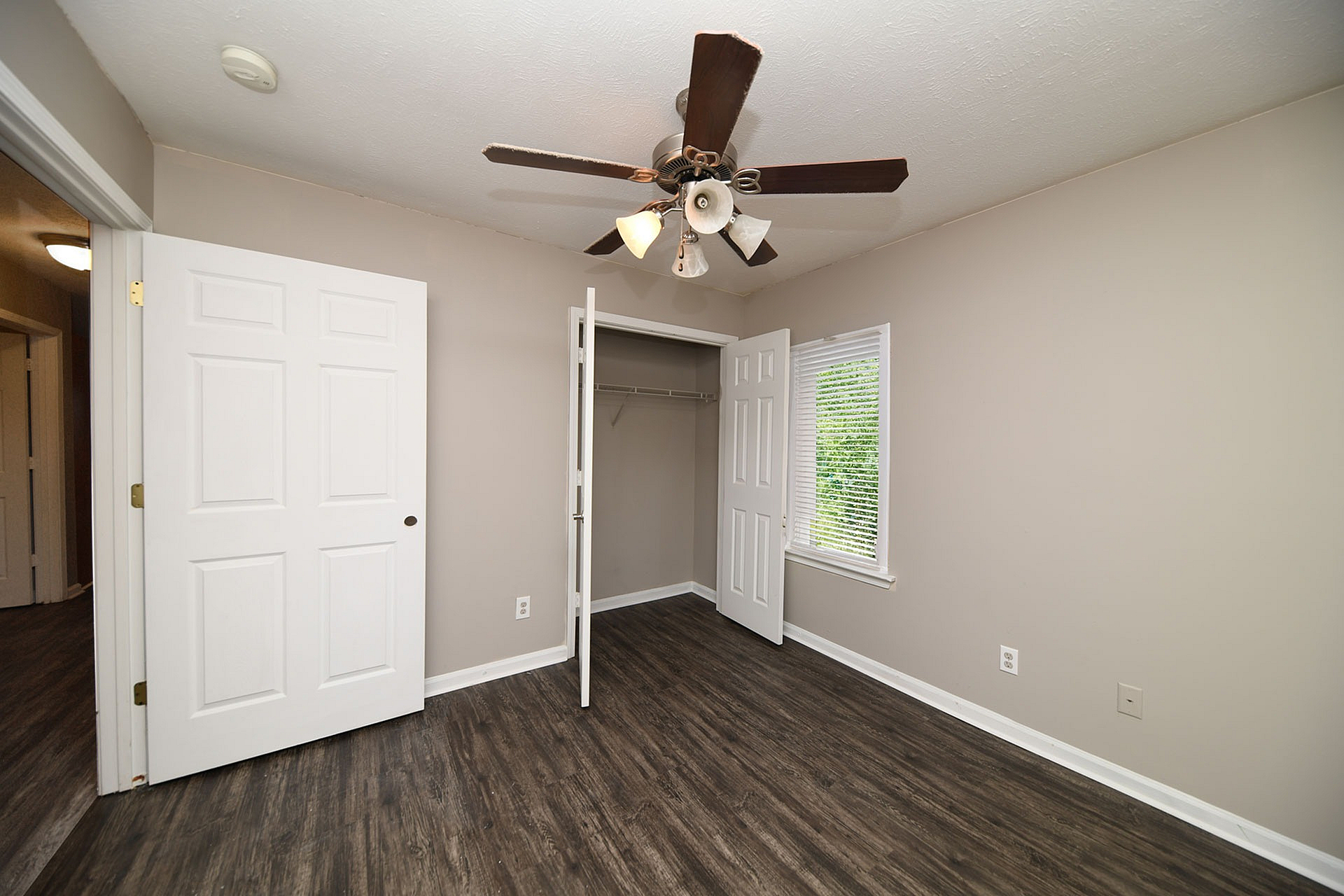 Chic bedroom with elegant ceiling fan, wooden flooring, and ample closet space for comfortable living.