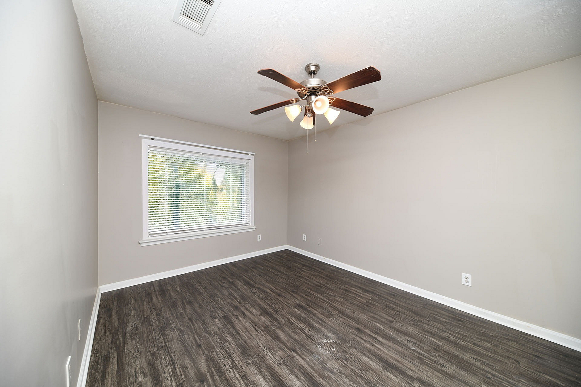 Bright, spacious room with elegant wood flooring and modern ceiling fan, ideal for a serene home environment.