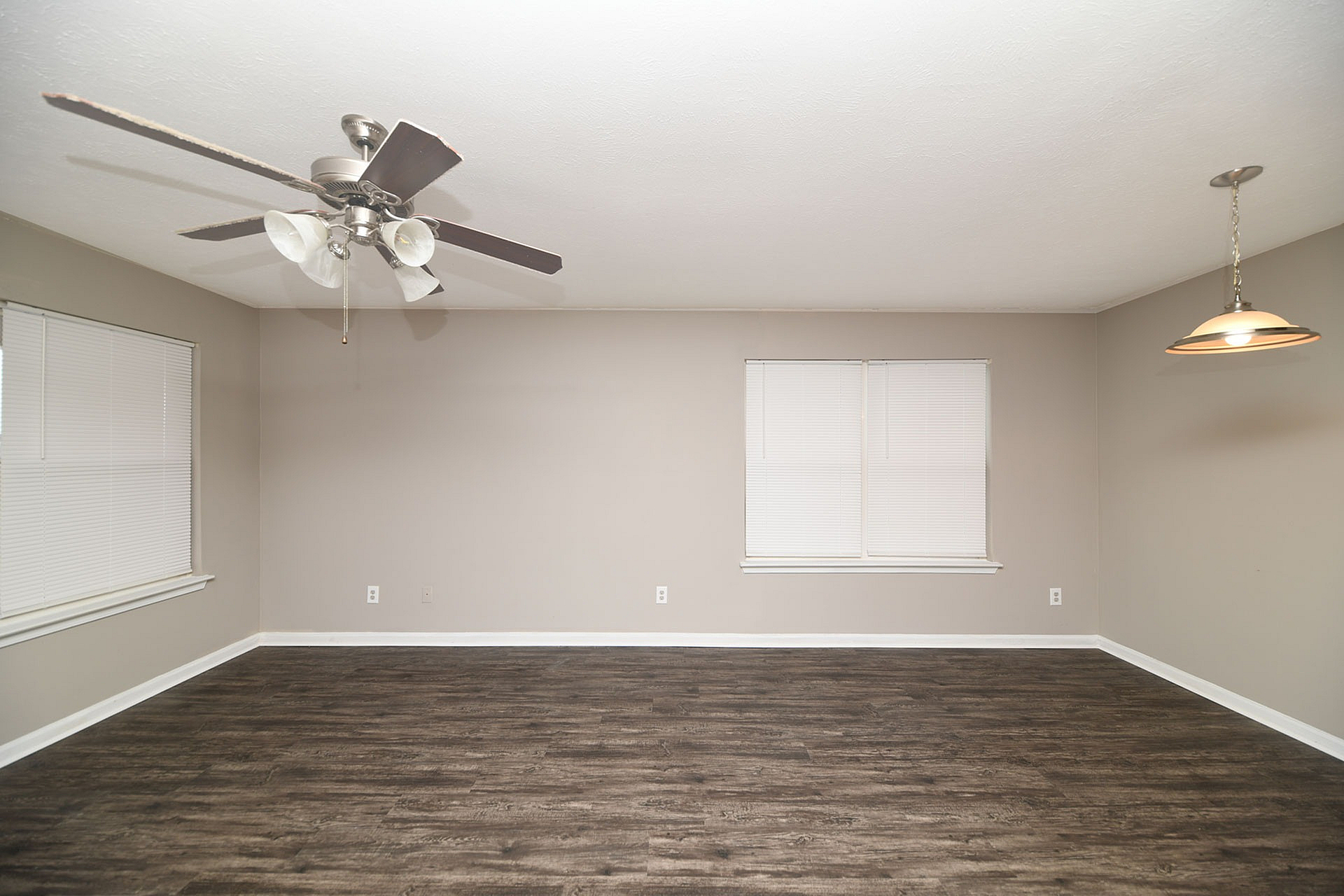 Spacious living room with elegant wood flooring, modern ceiling fan, and chic lighting fixture, perfect for entertaining.