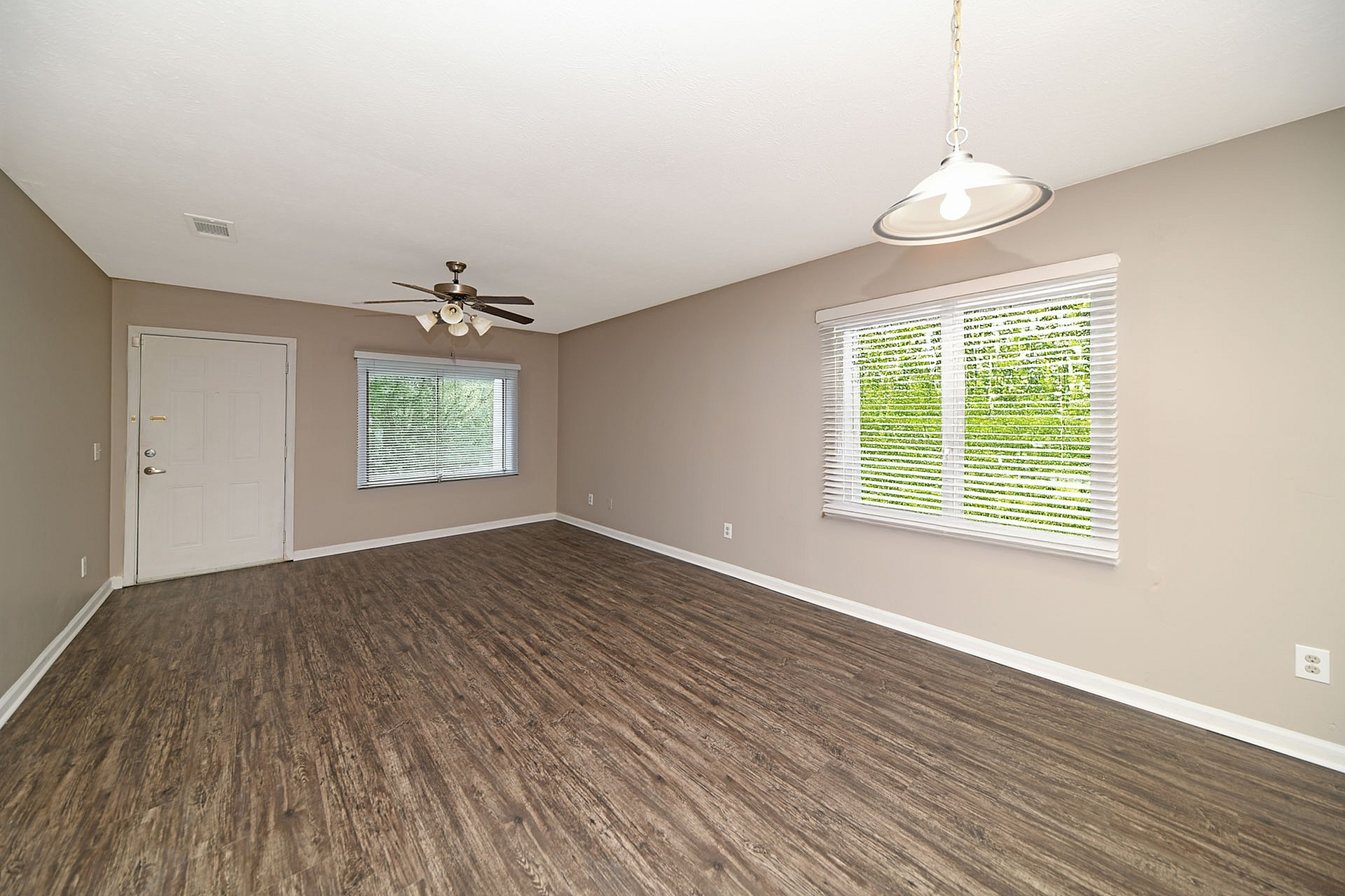 Bright and spacious living area with elegant hardwood floors, large windows, and a modern ceiling fan, creating a warm and inviting atmosphere.
