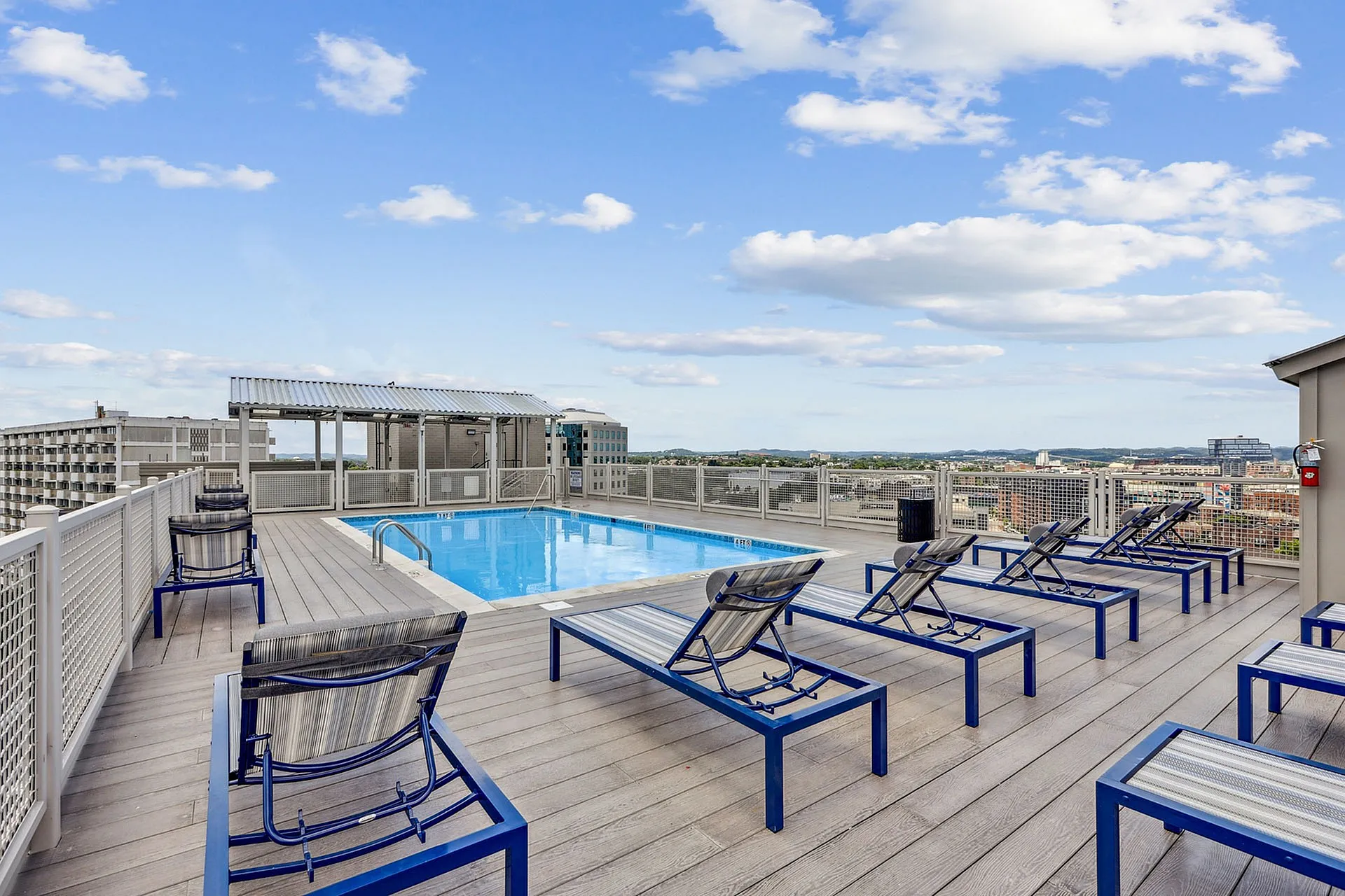 Stunning rooftop pool with modern lounge chairs offering panoramic city views under a vibrant blue sky.