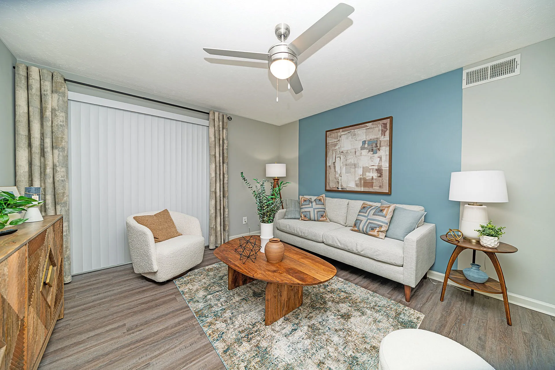 Chic and inviting living room with modern decor, featuring a cozy white armchair, stylish wooden coffee table, and a contemporary sofa set against a soothing blue accent wall.