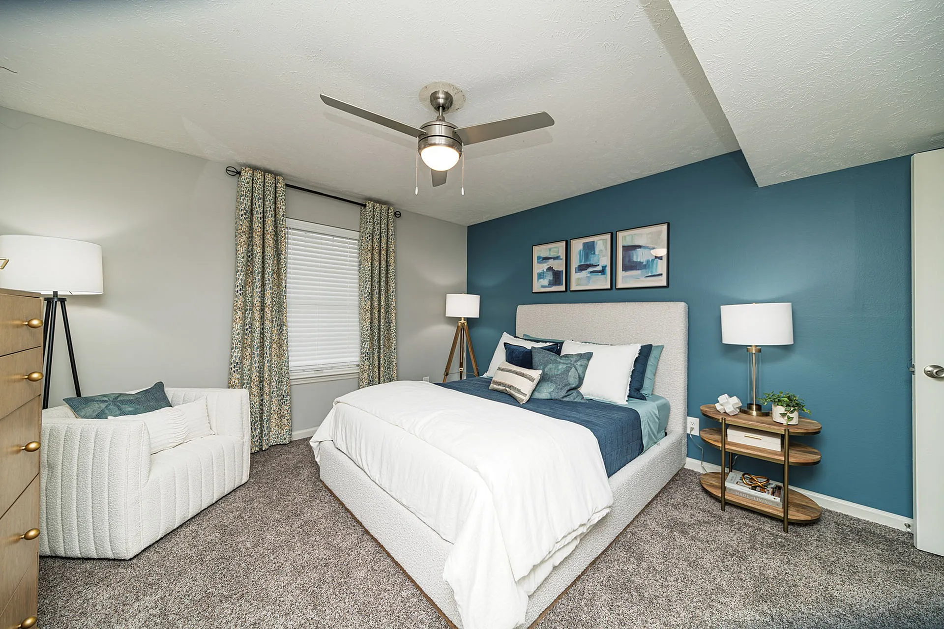 Cozy bedroom with modern decor, featuring a plush bed, stylish lighting, and chic artwork on a teal accent wall.