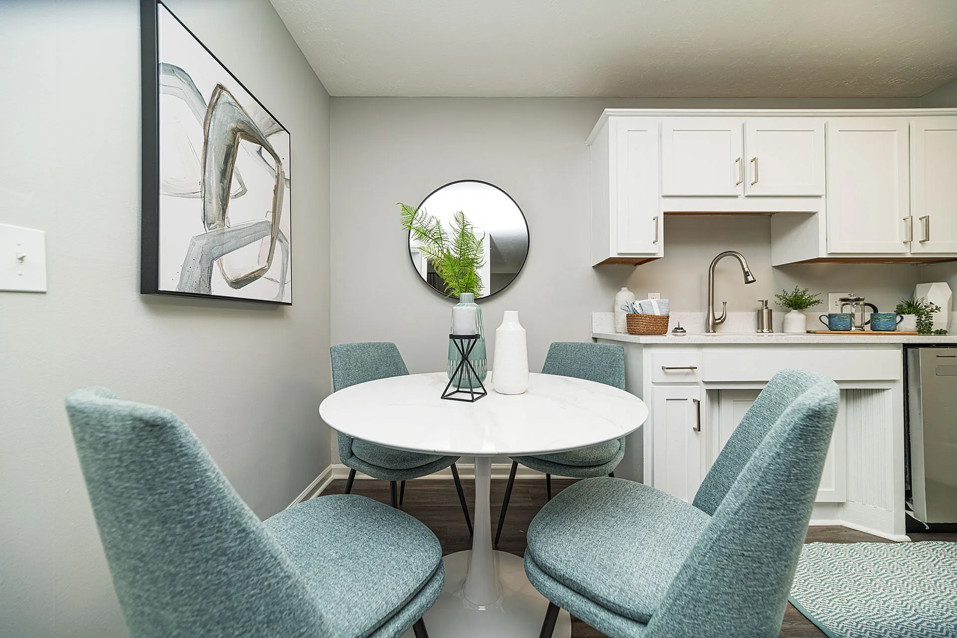 Chic dining nook featuring modern white cabinetry, a sleek round table, and stylish teal chairs, perfect for cozy gatherings.