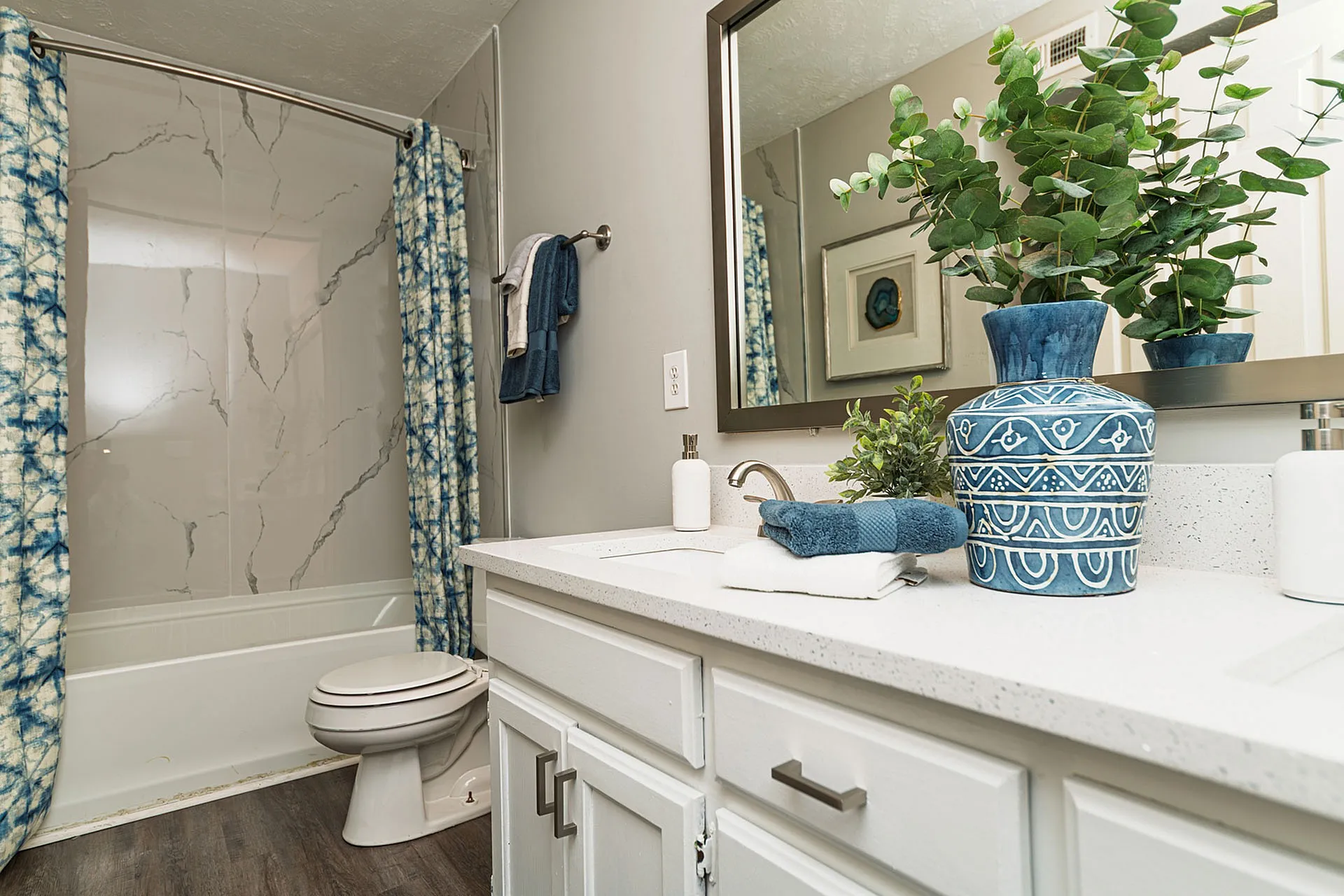 Chic bathroom featuring a marble-patterned shower, elegant white countertop, and stylish blue accents with lush greenery.