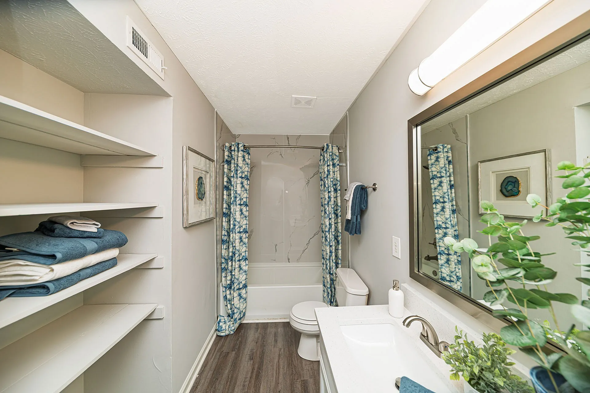 Inviting bathroom with modern decor, featuring elegant marble tiles, stylish blue patterned shower curtain, and lush greenery for a refreshing ambiance.