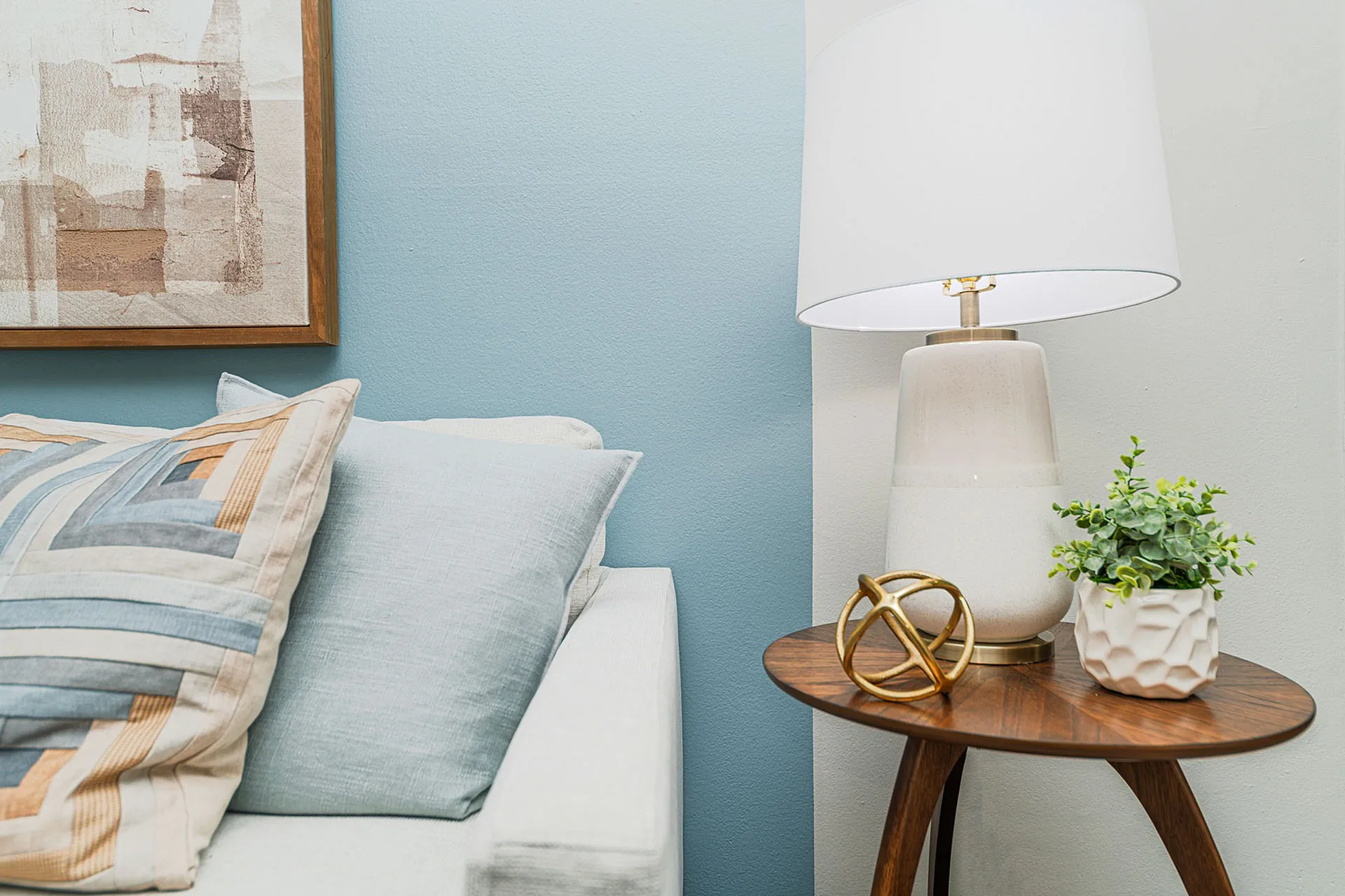Chic living space with modern decor featuring an elegant wood side table, stylish lamp, abstract art, and cozy cushions in a cool-toned setting.