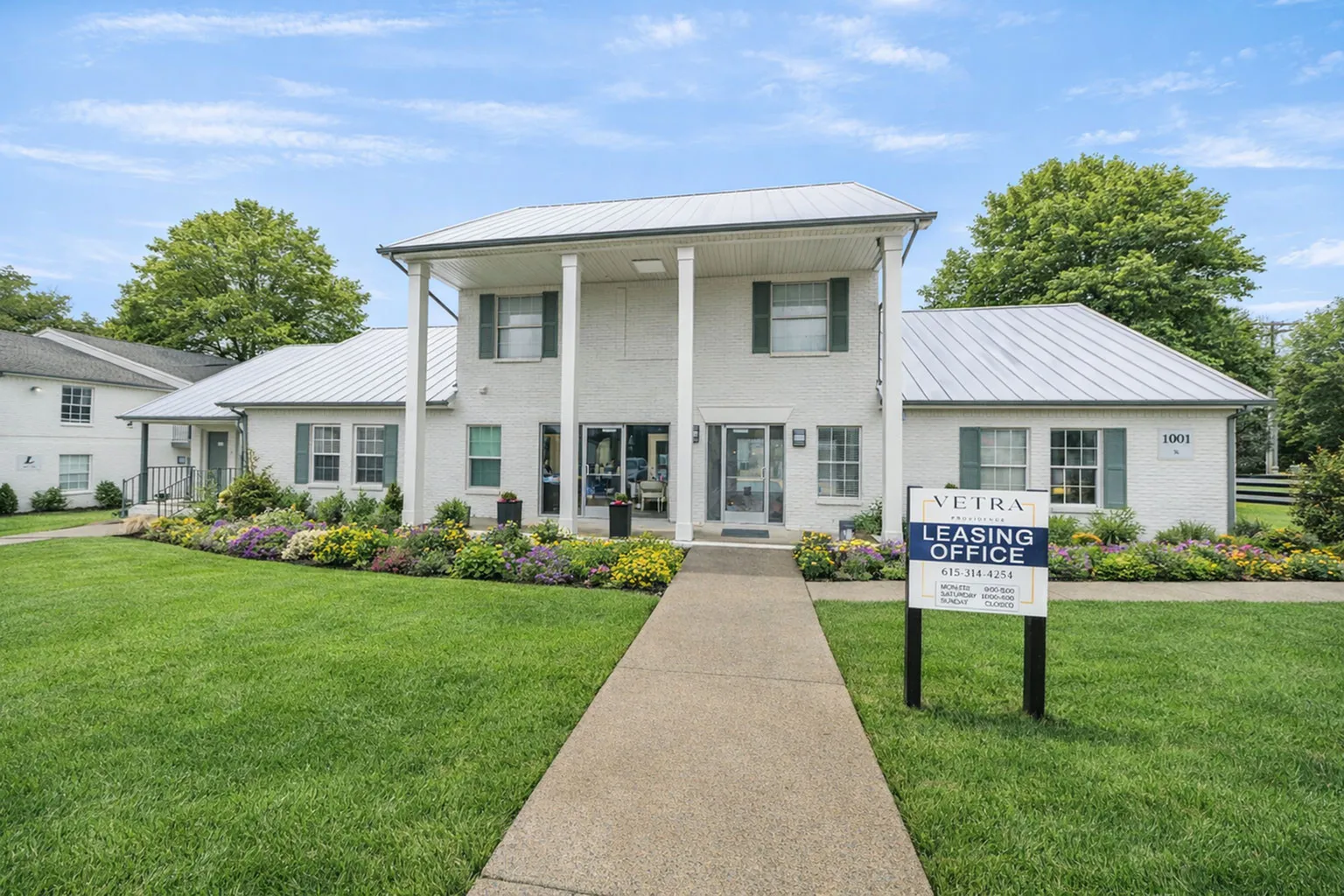 Charming leasing office with a welcoming walkway, surrounded by lush greenery and colorful flowers, indicating a vibrant community atmosphere.