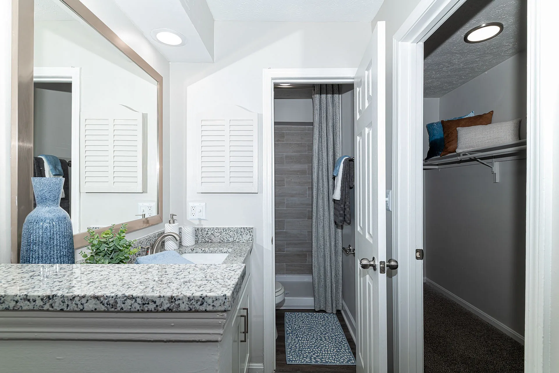 Chic bathroom with elegant granite countertop, framed mirror, and inviting walk-in closet for luxury living.