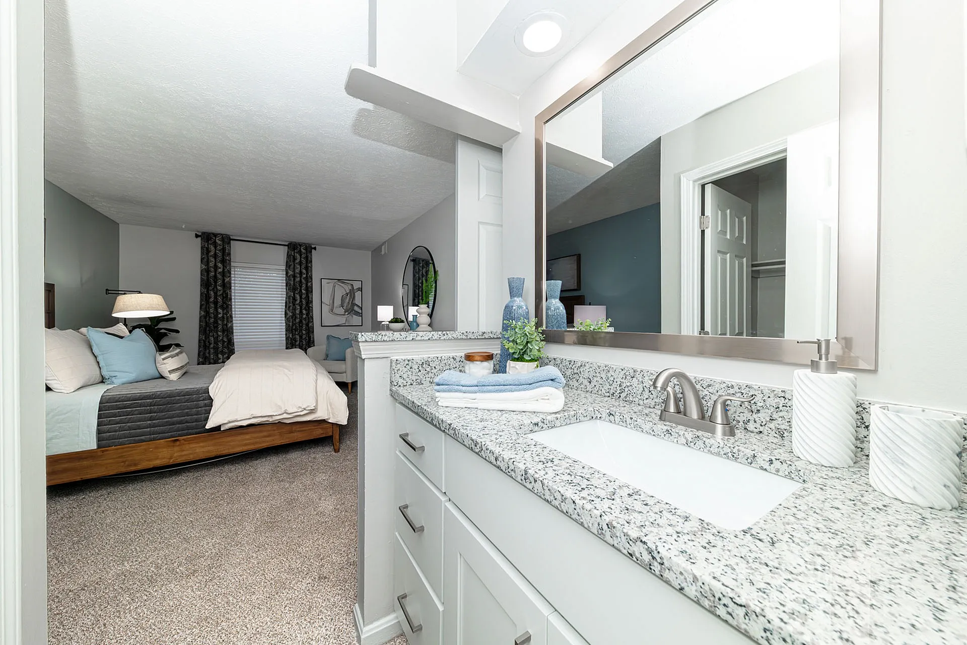 Elegant bedroom with plush carpeting and adjoining bathroom featuring granite countertops and sleek fixtures.