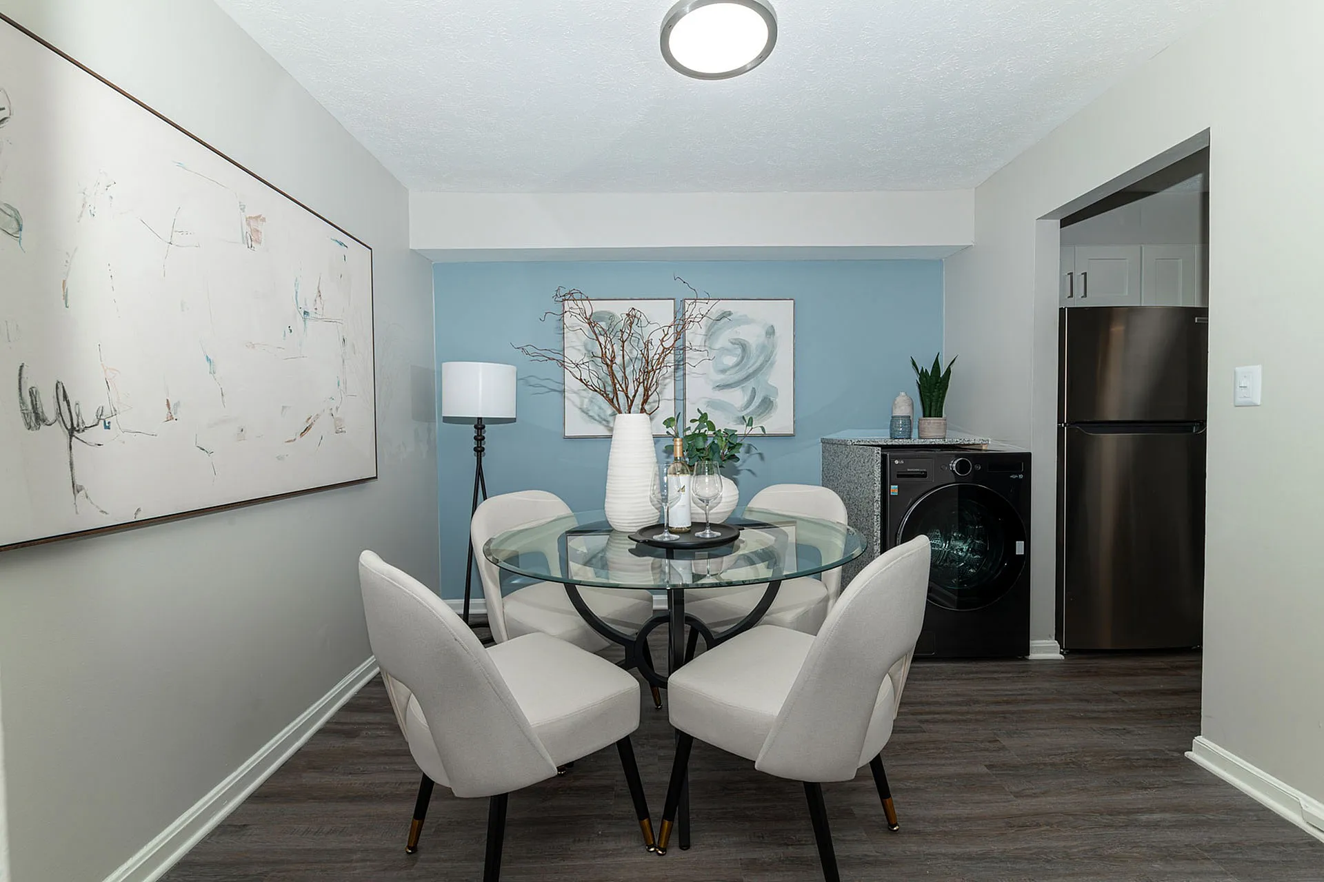 Chic dining area with elegant glass table and modern decor, complemented by a stylish blue accent wall.