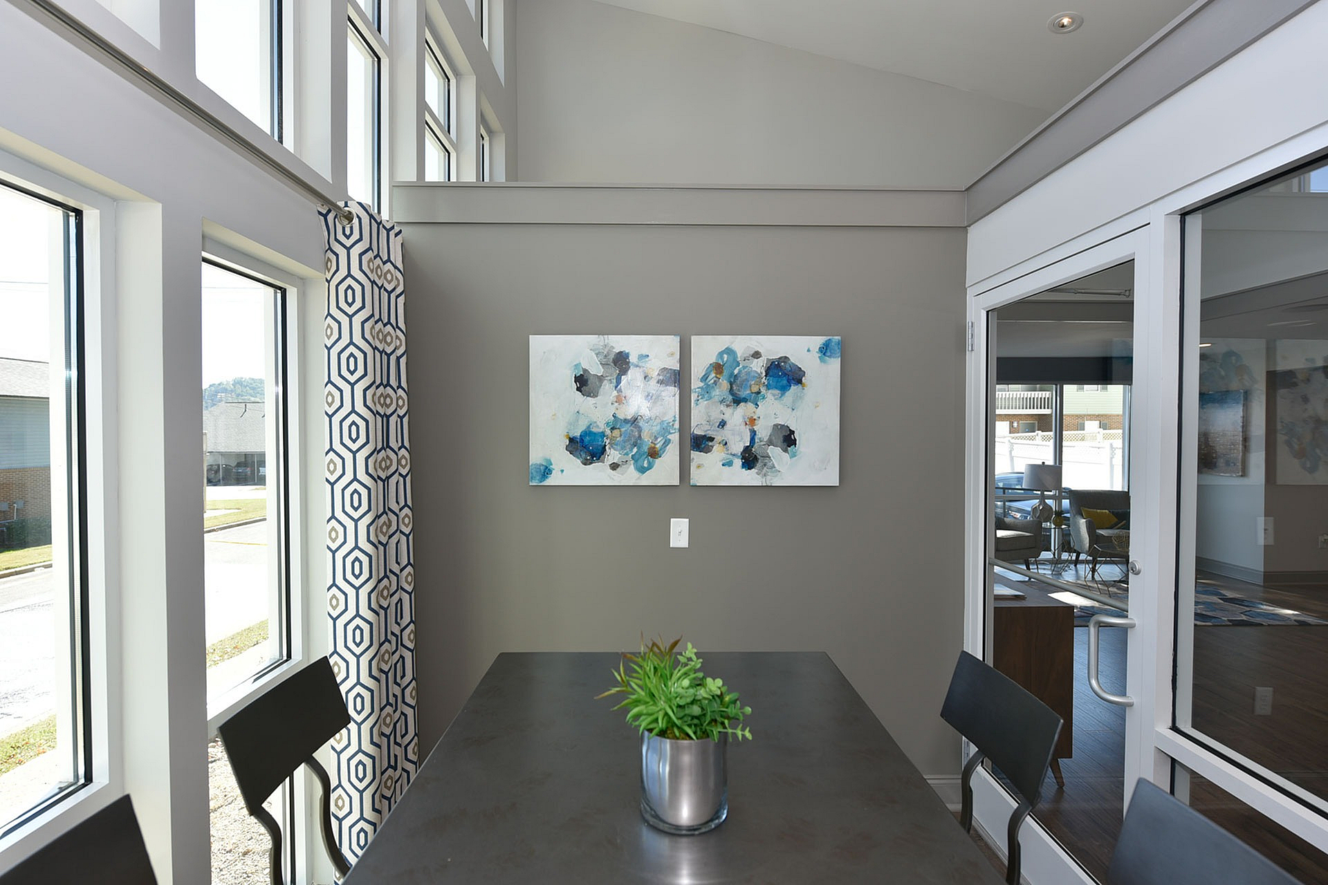 Modern dining area with large windows, stylish geometric curtains, and contemporary artwork, offering abundant natural light.