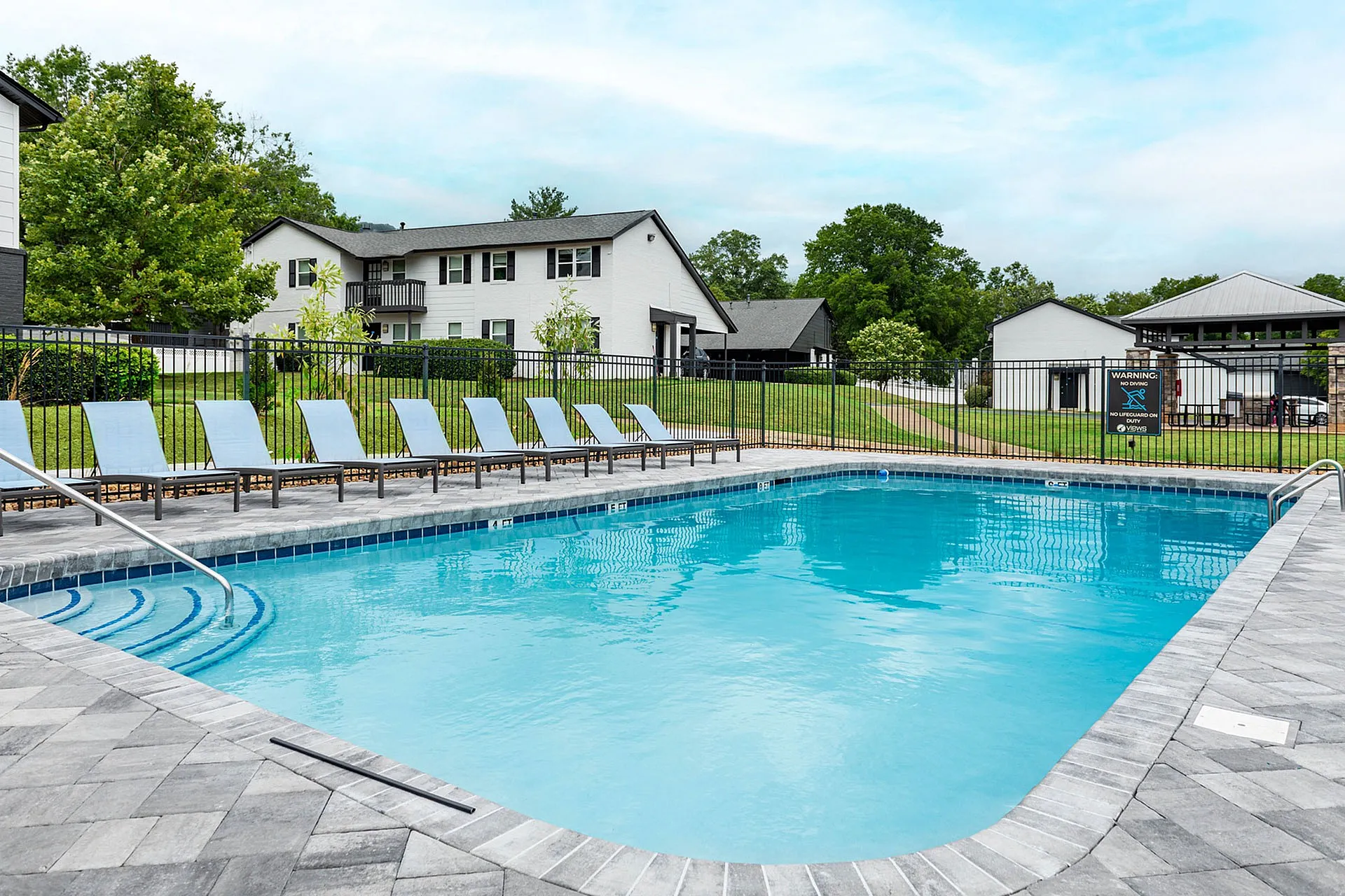 Inviting outdoor pool area with comfortable lounge chairs, surrounded by lush greenery and modern residential buildings.
