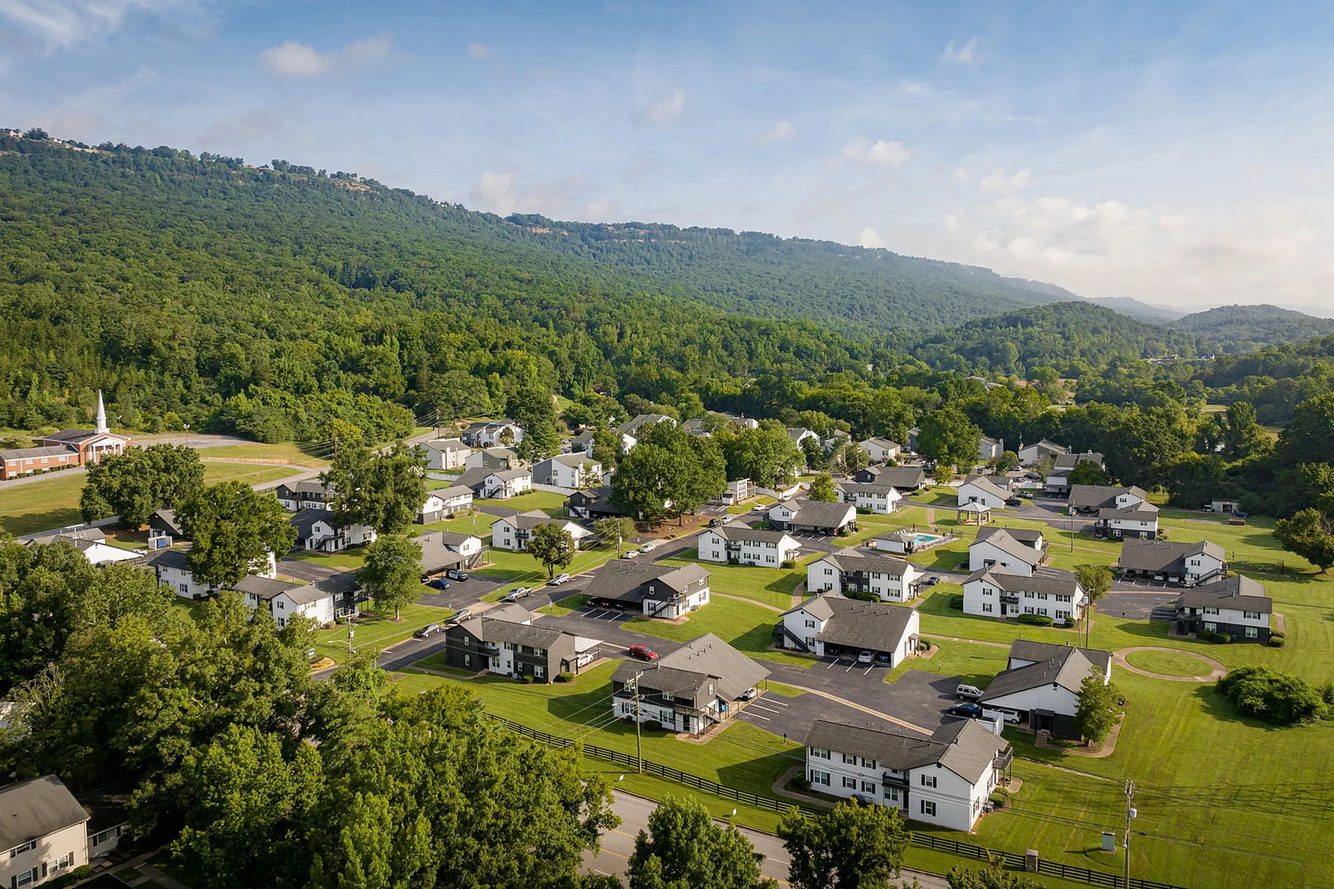 Charming aerial view of a picturesque neighborhood nestled among lush green hills, showcasing cozy homes and tranquil surroundings.