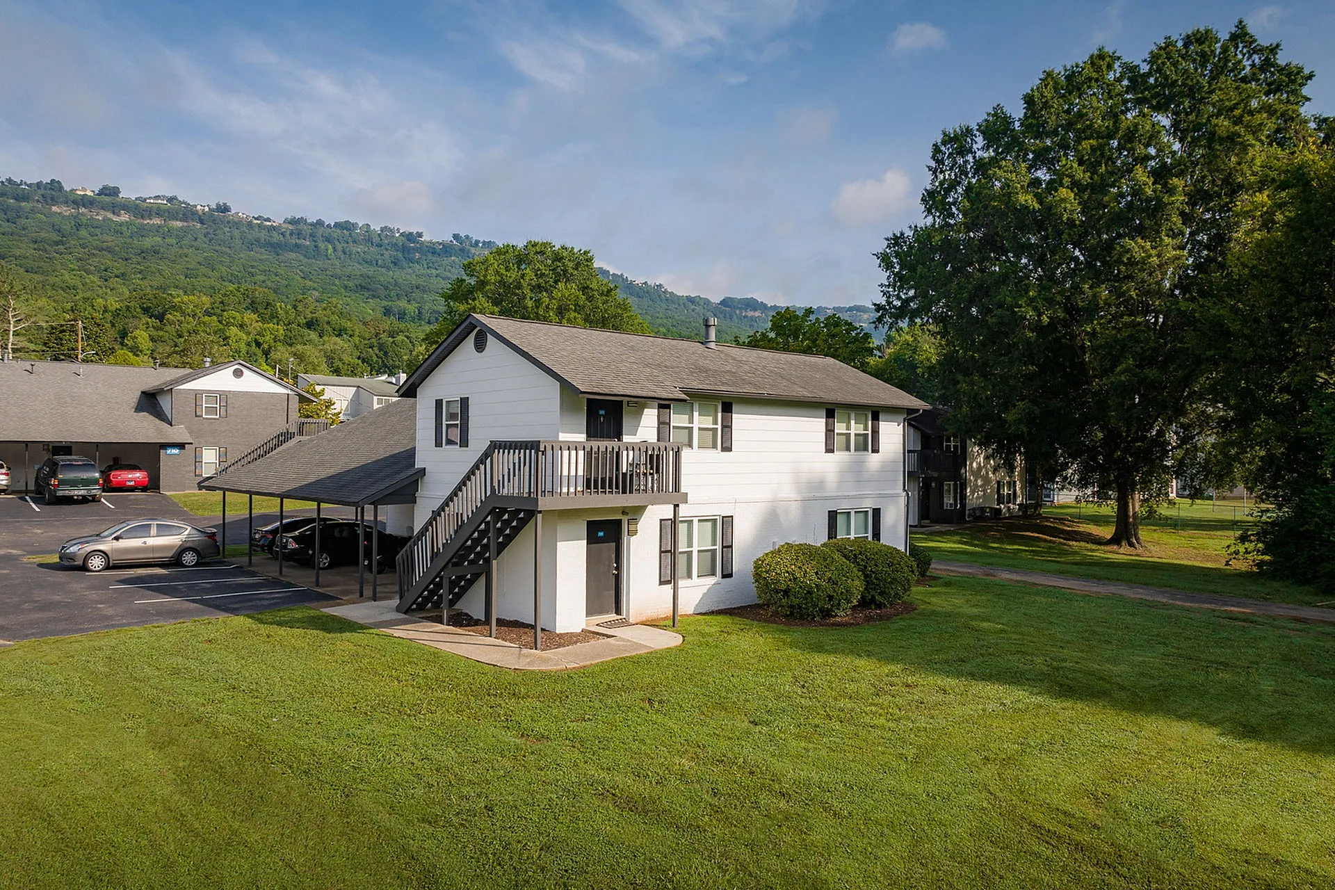 Charming two-story apartment building nestled in a lush green landscape with scenic mountain views, ample parking, and serene surroundings.