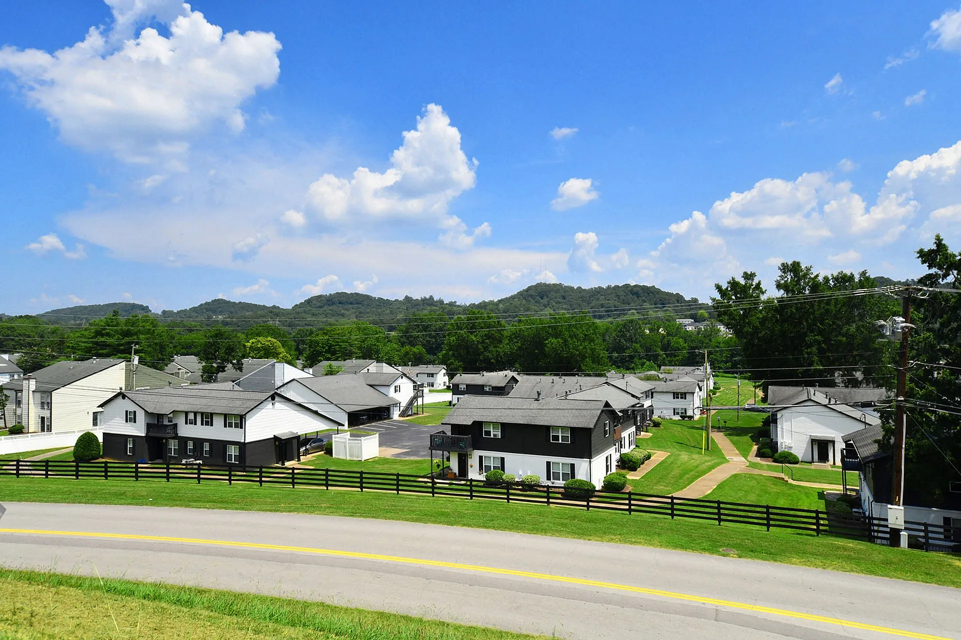 Charming residential neighborhood with picturesque homes, surrounded by lush greenery and rolling hills under a vibrant blue sky.