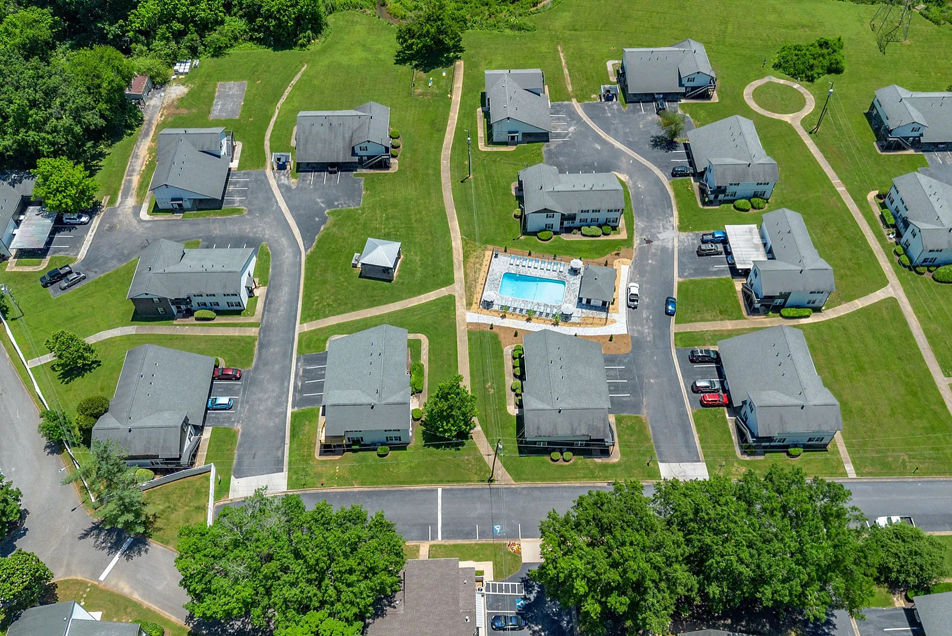 Aerial view of a charming apartment complex with lush green lawns, a central swimming pool, and convenient walking paths.