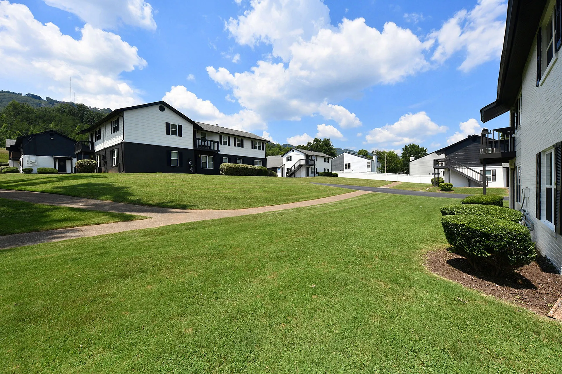 Charming apartment complex with well-manicured lawns, surrounded by scenic greenery and bright blue skies.