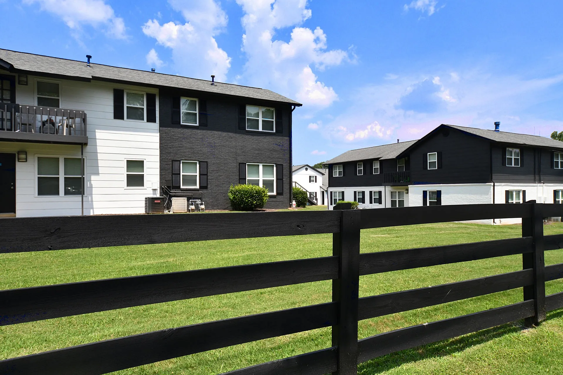 Charming modern apartments with sleek black and white facades, lush green lawns, and a serene blue sky backdrop.