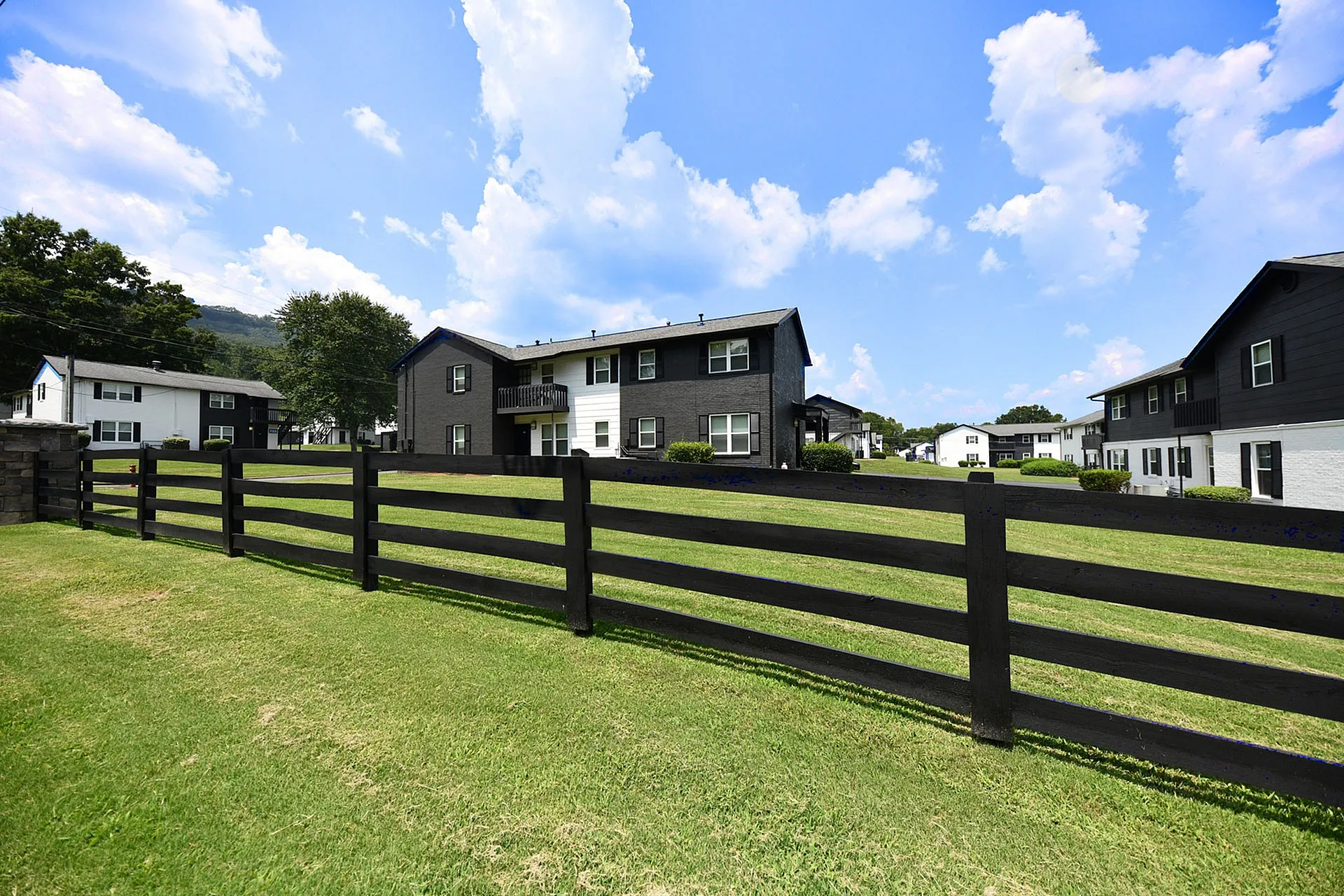 Charming residential community featuring stylish two-story buildings and lush green lawns, set under a bright blue sky.