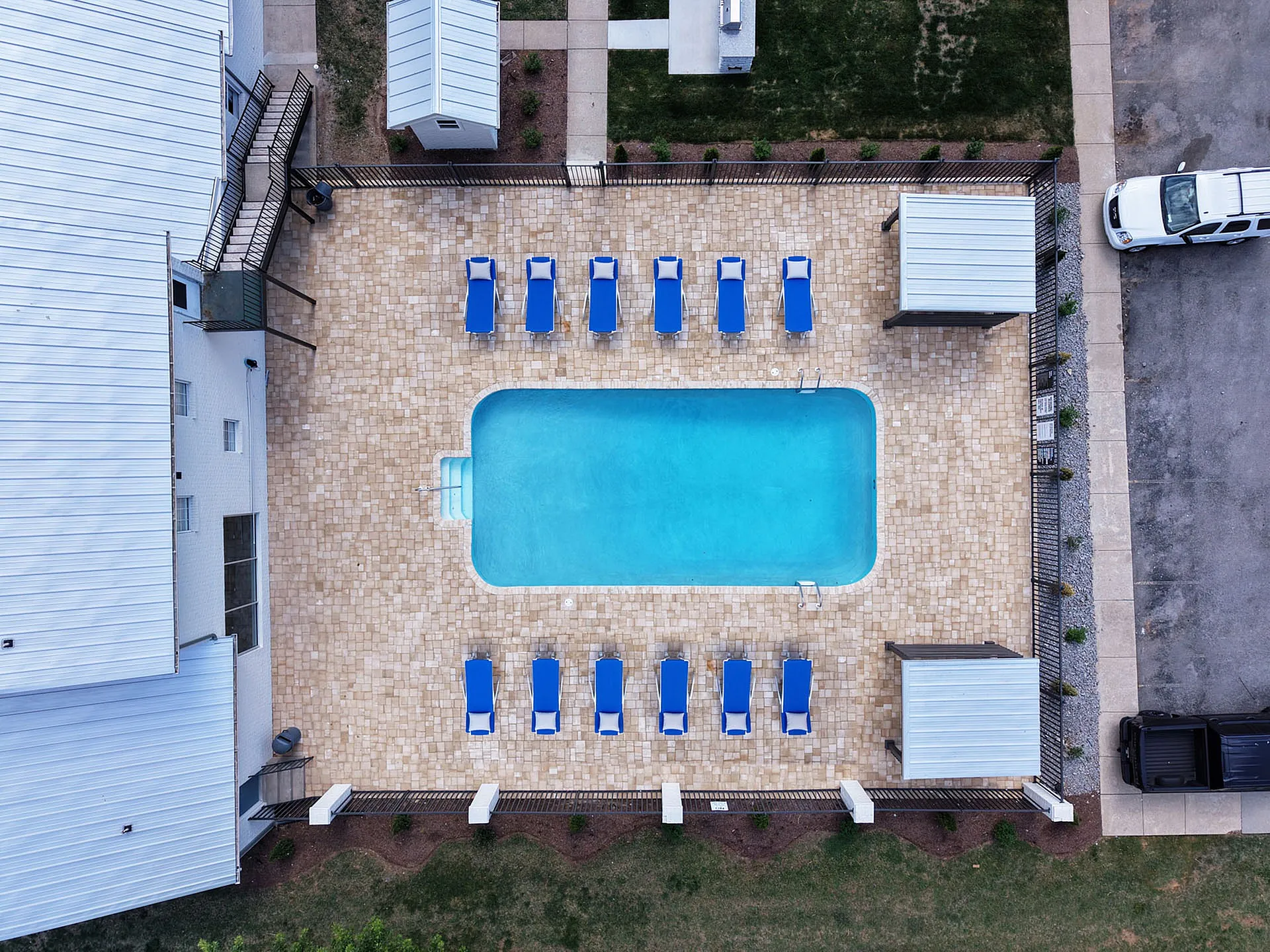 Inviting aerial view of a modern apartment complex featuring a pristine swimming pool surrounded by sun loungers and shaded cabanas, perfect for relaxation.