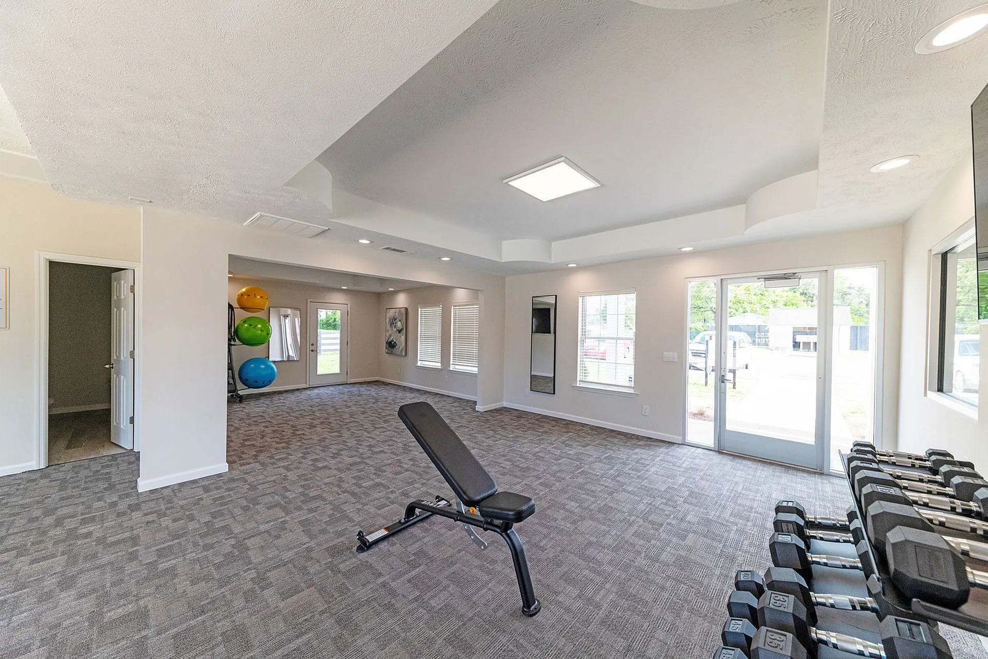 Bright, modern gym space with large windows, fitness ball stack, weights, and multifunctional bench.
