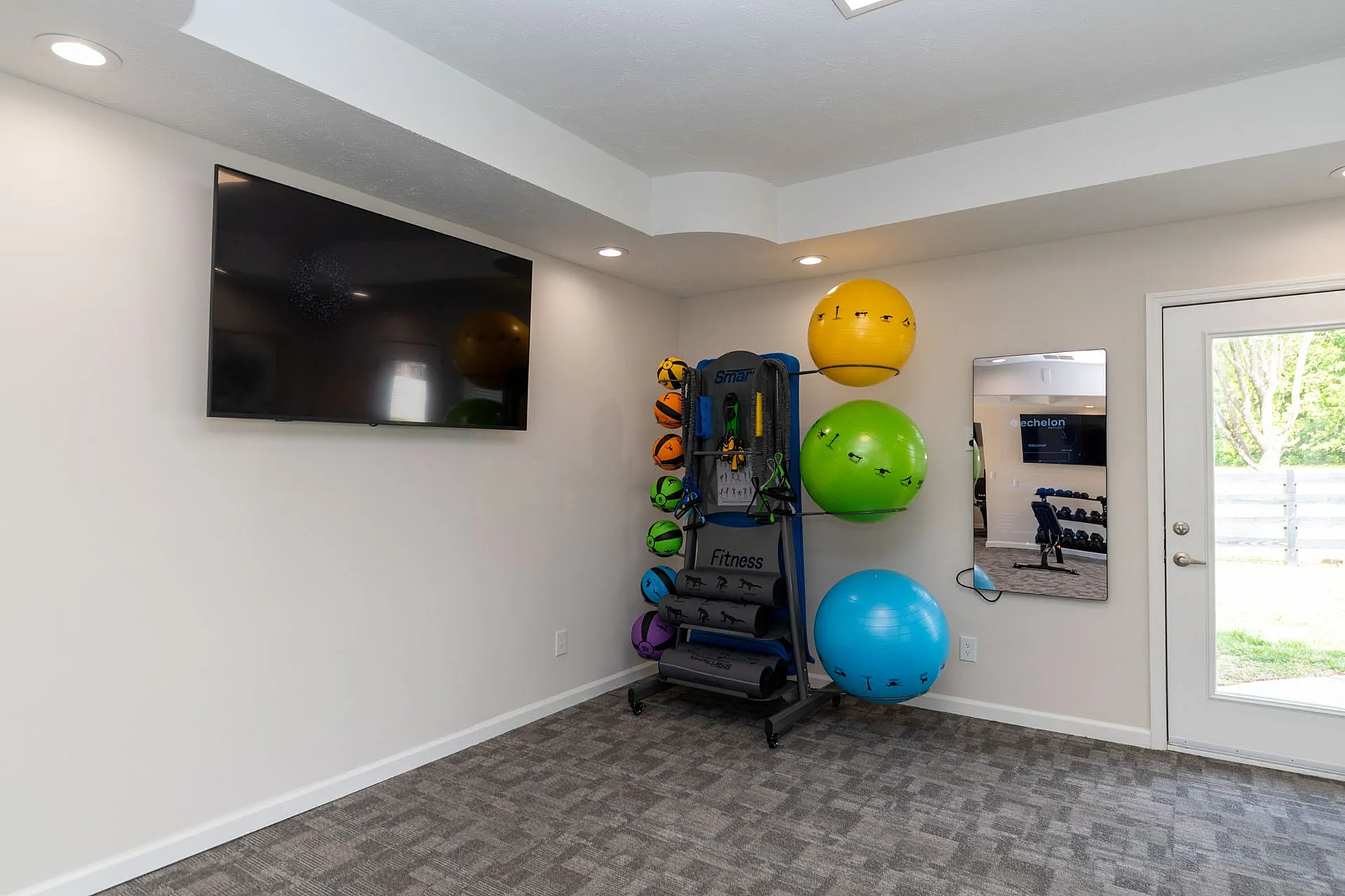Modern fitness room with exercise balls, smart fitness equipment, and a large mirror, perfect for home workouts.