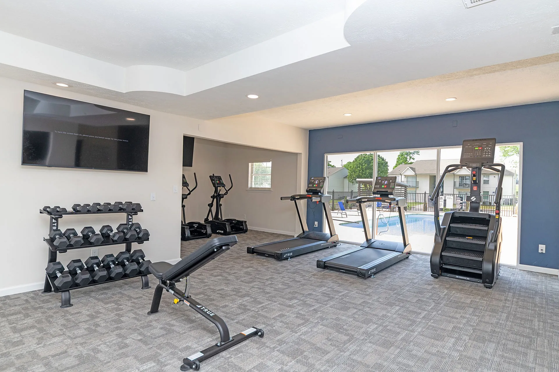 Modern gym with state-of-the-art exercise equipment, including treadmills and weights, overlooking a refreshing pool area.