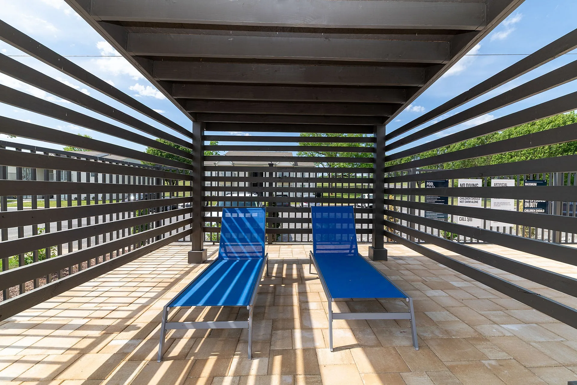 Contemporary outdoor patio with two sleek blue loungers under a stylish pergola, perfect for relaxing on a sunny day.