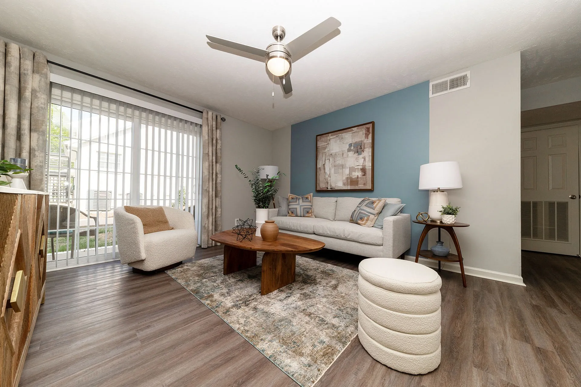 Inviting living room with a modern ceiling fan, stylish furniture, and natural light streaming through large sliding glass doors.