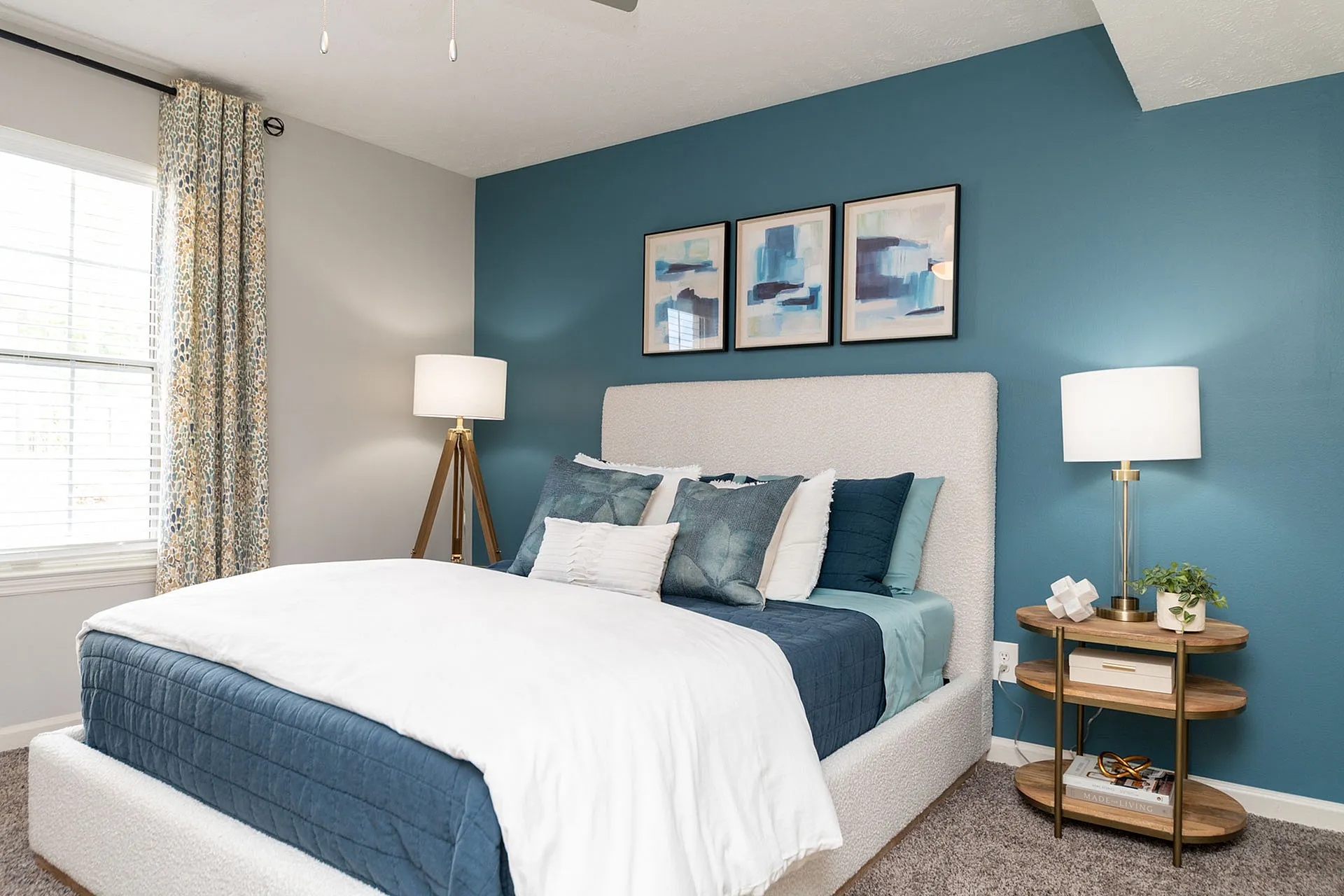 Modern bedroom with elegant blue accent wall, cozy white bed, stylish decor, and abundant natural light.