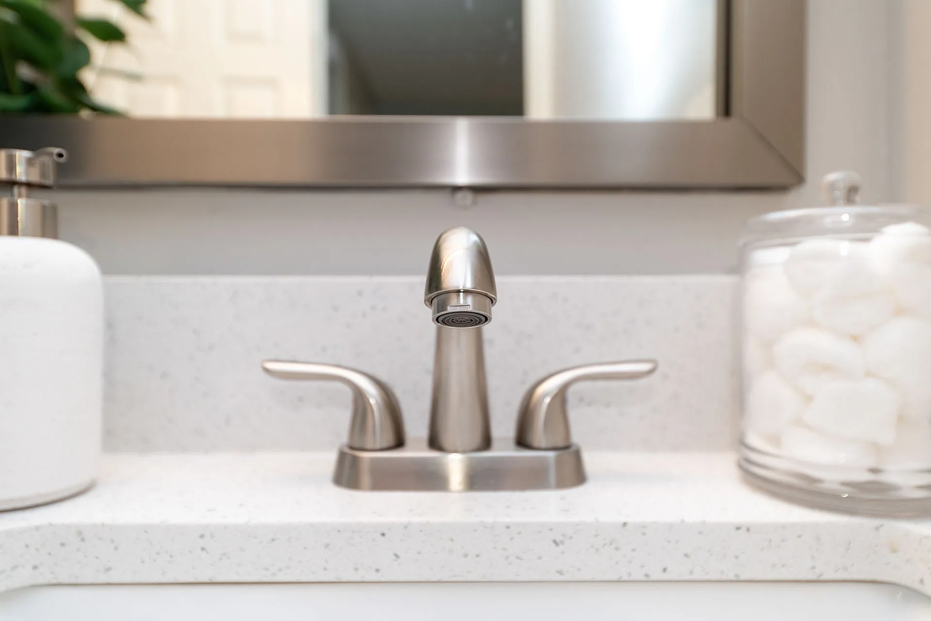 Sleek bathroom sink with elegant stainless steel faucet and modern marble countertop, complemented by a stylish glass container with plush cotton balls.