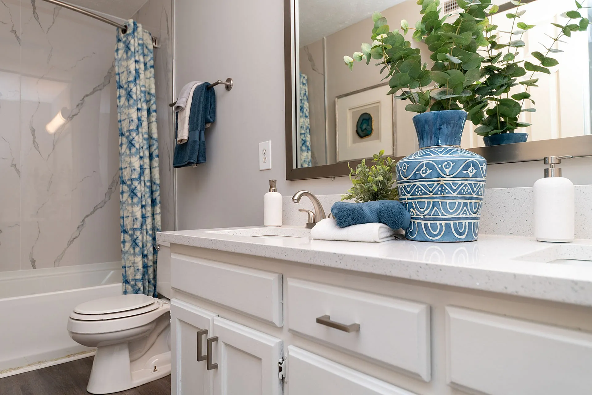 Elegant bathroom with modern decor featuring a sleek white countertop, blue patterned vase, and vibrant greenery adding a refreshing touch.