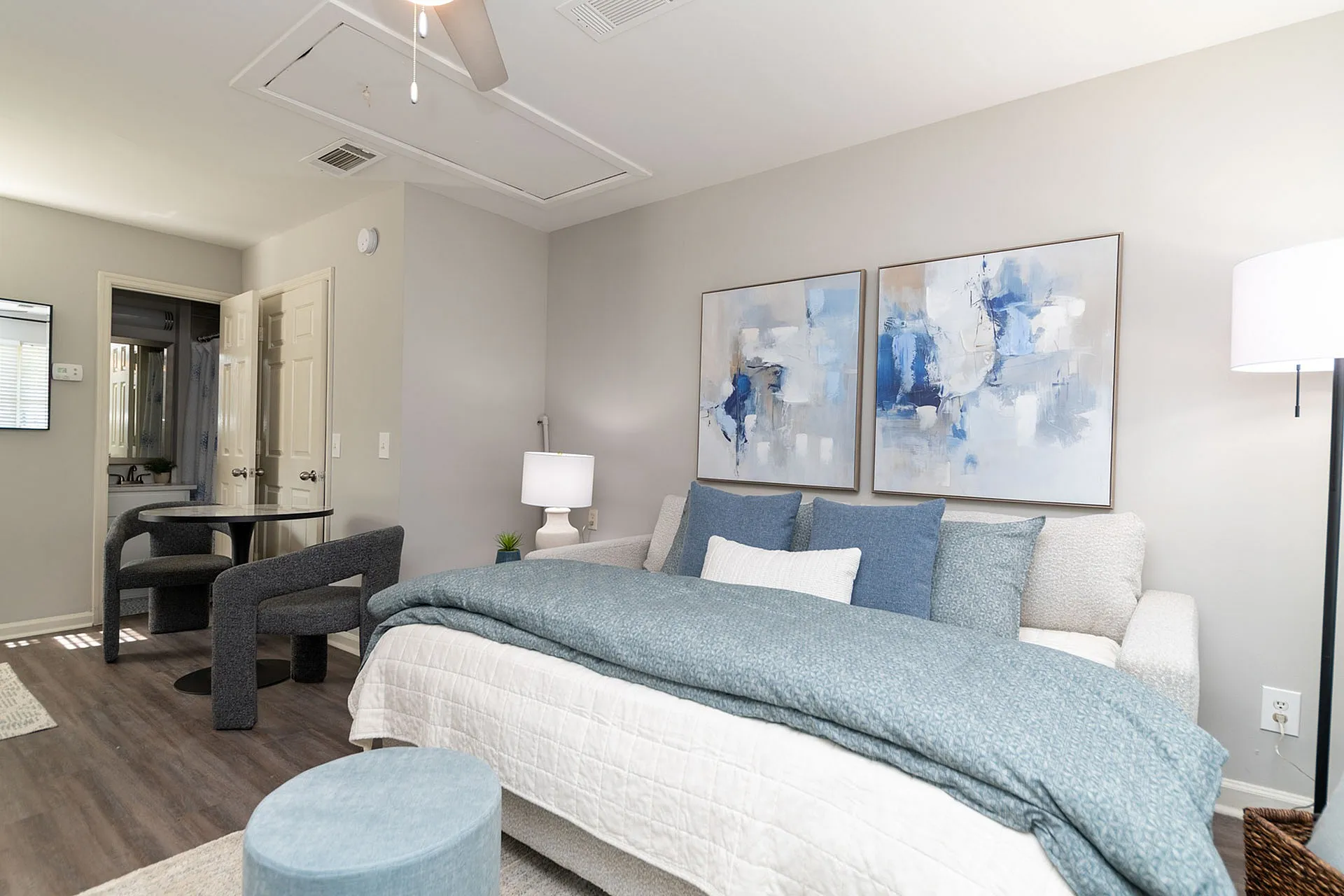 Cozy modern bedroom with stylish decor, featuring a plush bed, abstract art, and a cozy seating area perfect for relaxation.