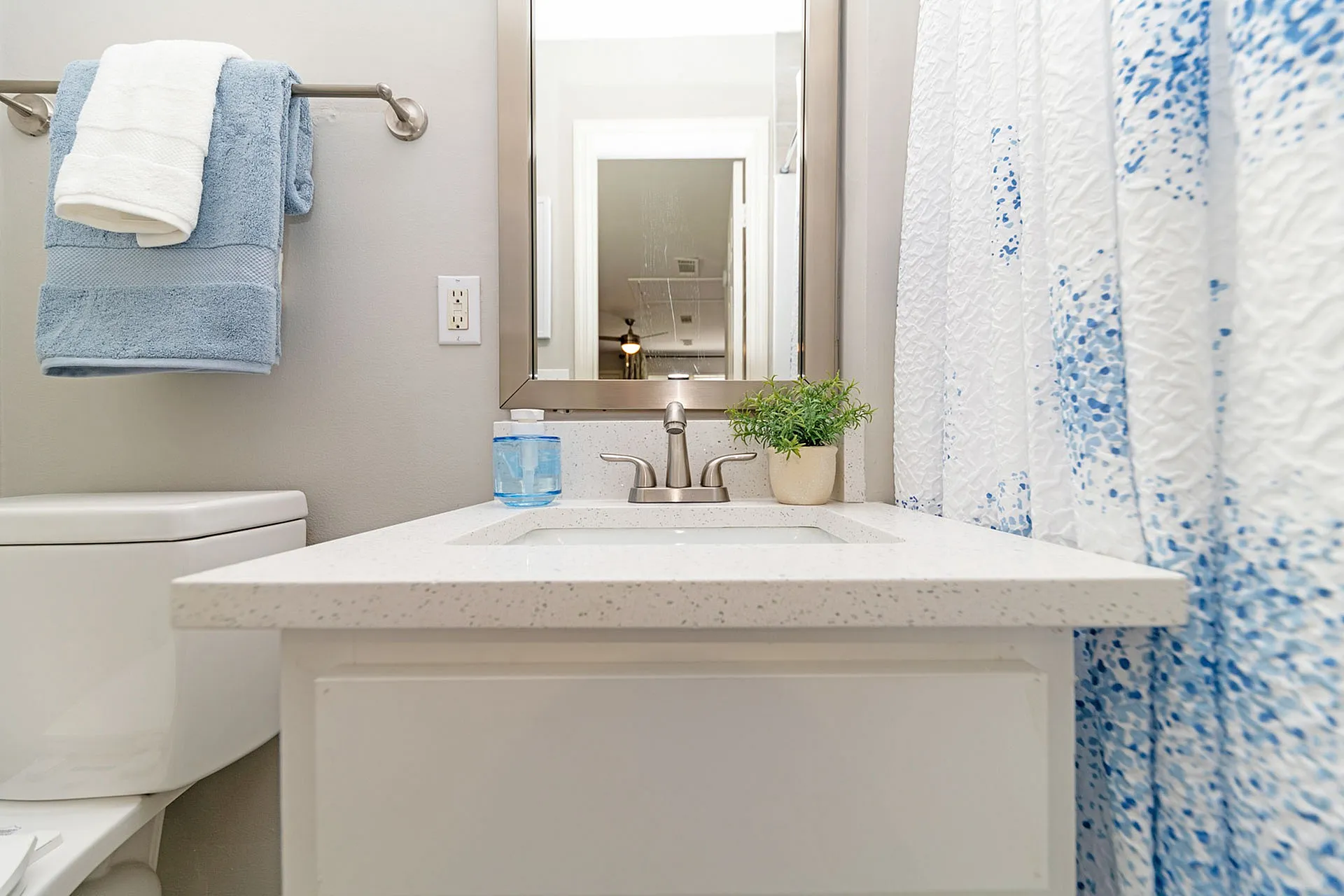 Bright and modern bathroom with sleek white countertop, elegant fixtures, and a stylish blue-and-white shower curtain.