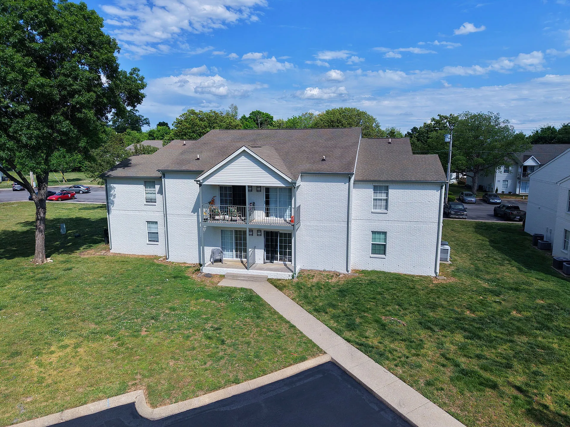 Charming two-story apartment building surrounded by lush green lawns and trees, offering a tranquil residential setting.