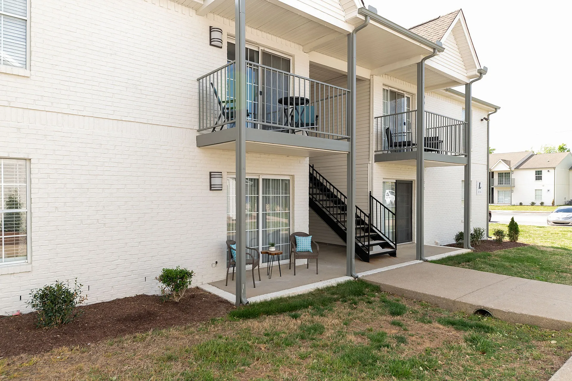 Charming apartment exterior featuring private balconies and cozy patios with modern seating, surrounded by well-maintained greenery and a peaceful neighborhood setting.