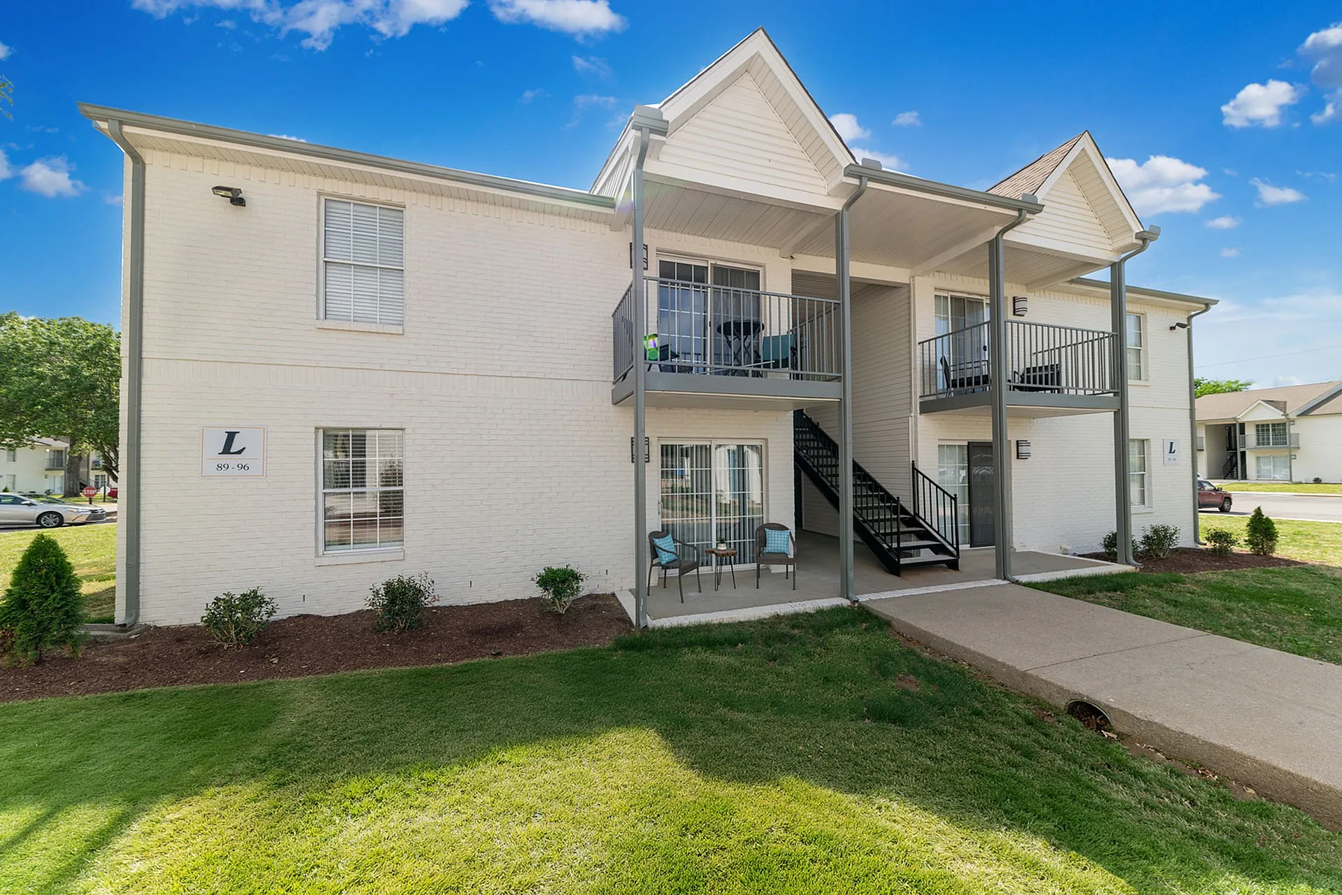 Charming two-story brick apartment building with balconies and lush landscaping under a bright blue sky.