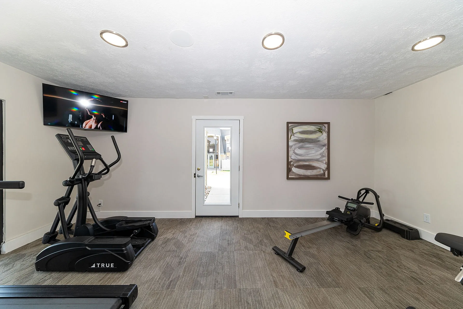 Modern home gym with sleek elliptical machine and rower, featuring a wall-mounted TV for an engaging workout experience.