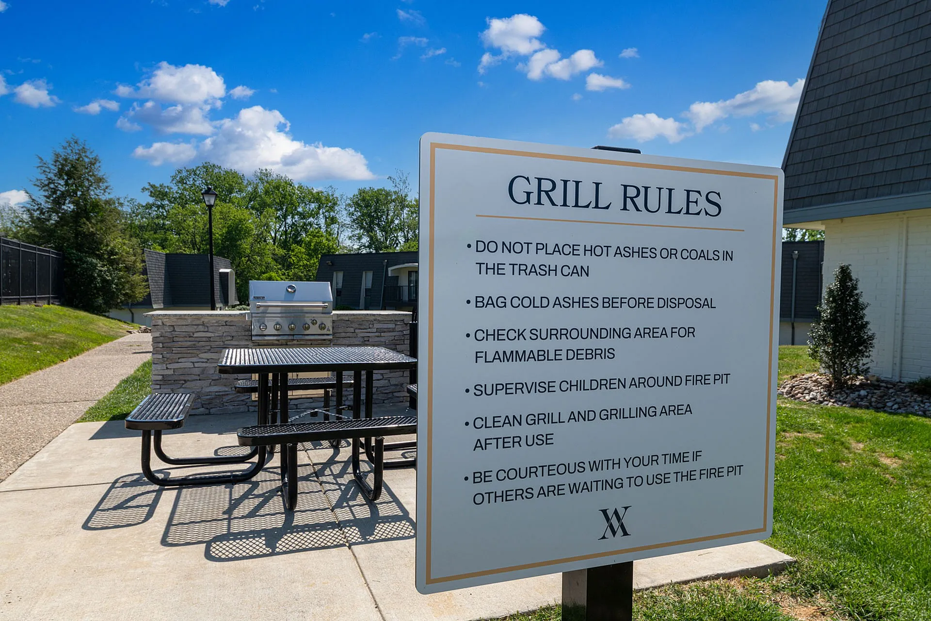 Inviting outdoor BBQ area with grill and picnic table set against a backdrop of clear blue skies and lush greenery.