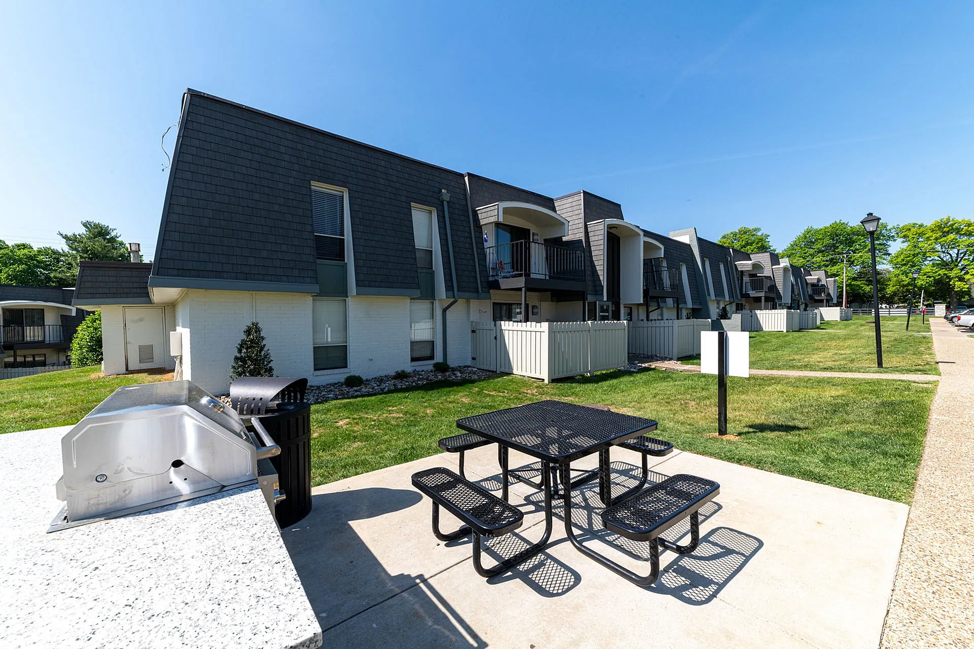 Modern apartment complex with stylish architecture, featuring outdoor picnic area and barbecue grill, surrounded by lush green lawns.