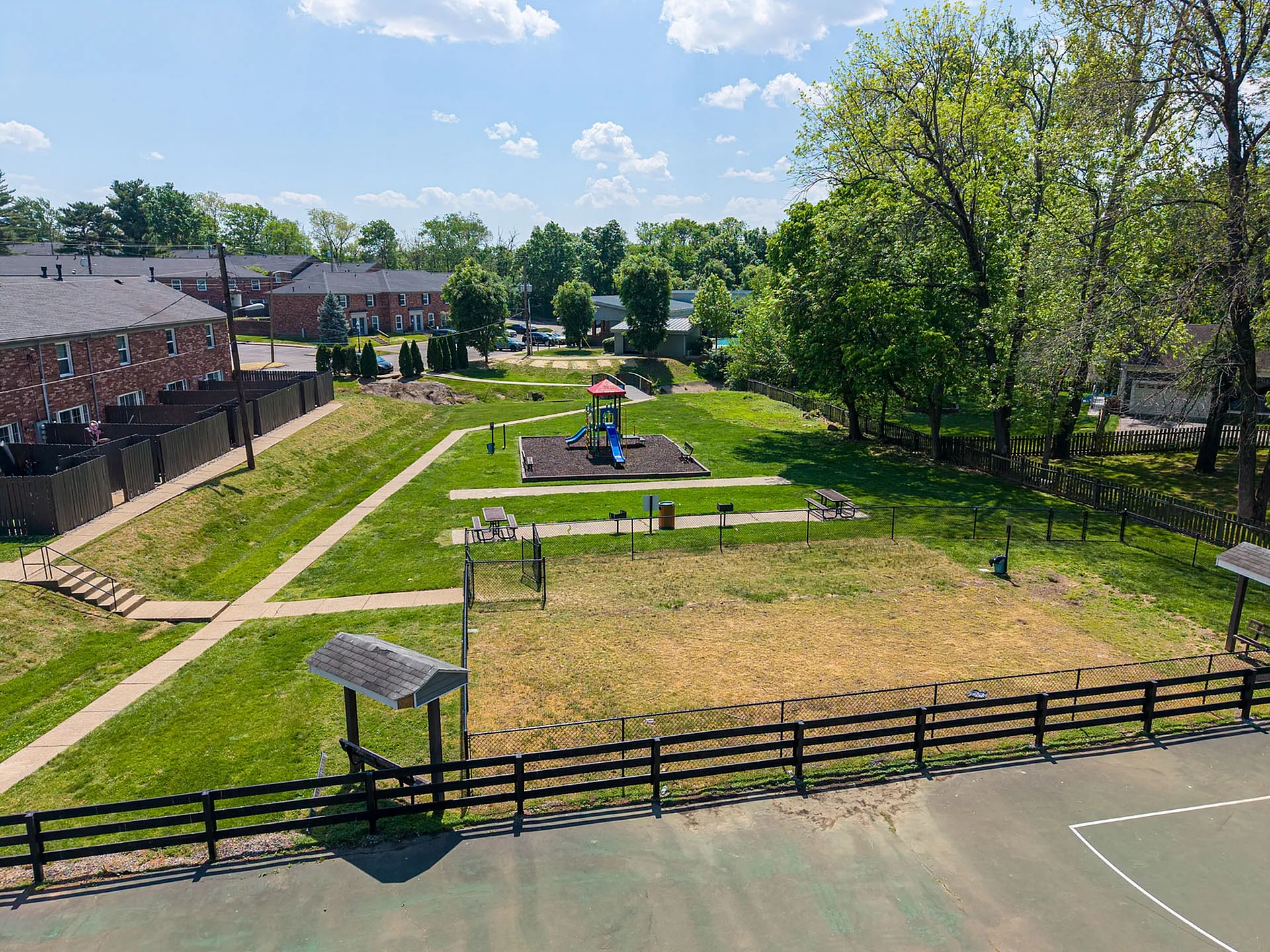 Charming park view with lush greenery, playground, picnic area, and adjacent brick townhouses in a serene neighborhood setting.