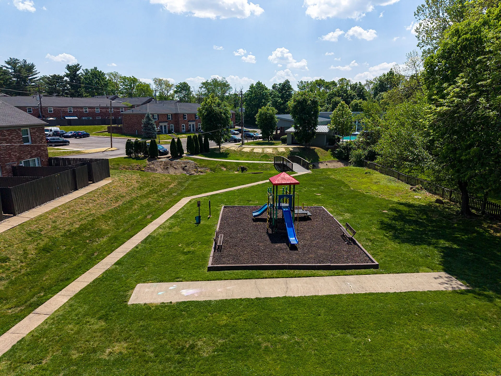 Charming community playground surrounded by lush greenery and quaint brick townhouses, perfect for family living.